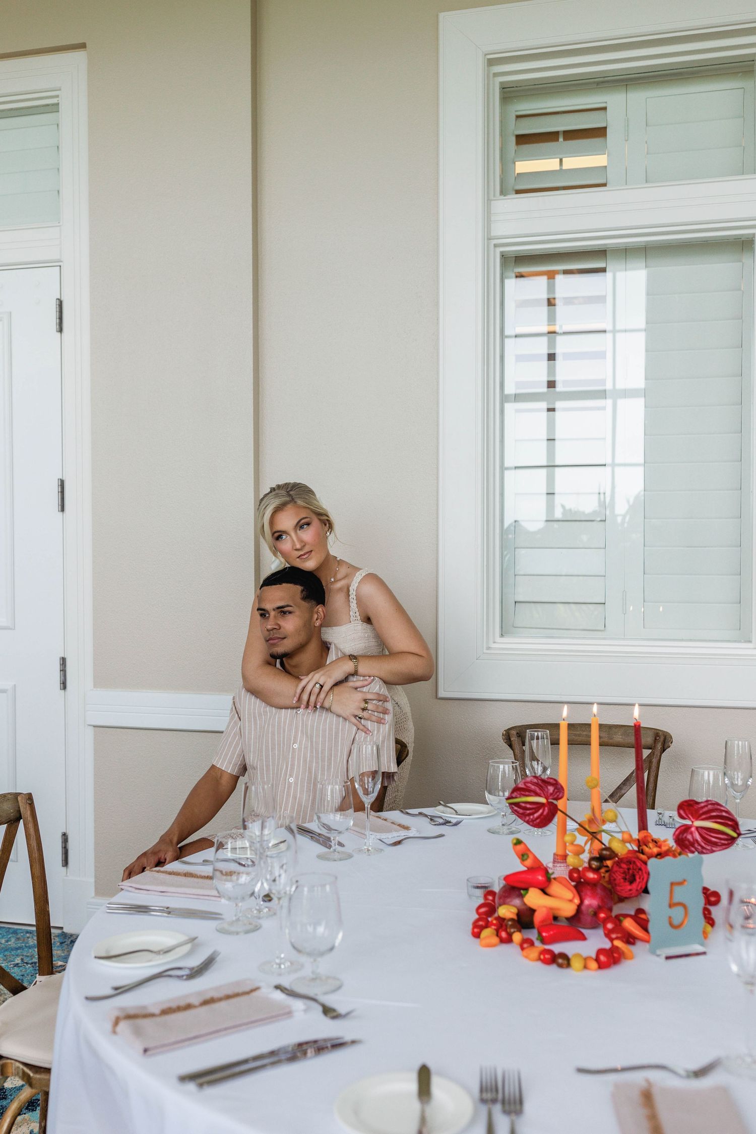 Elegant table setting with white linens and vibrant red floral centerpieces in a bright dining room.