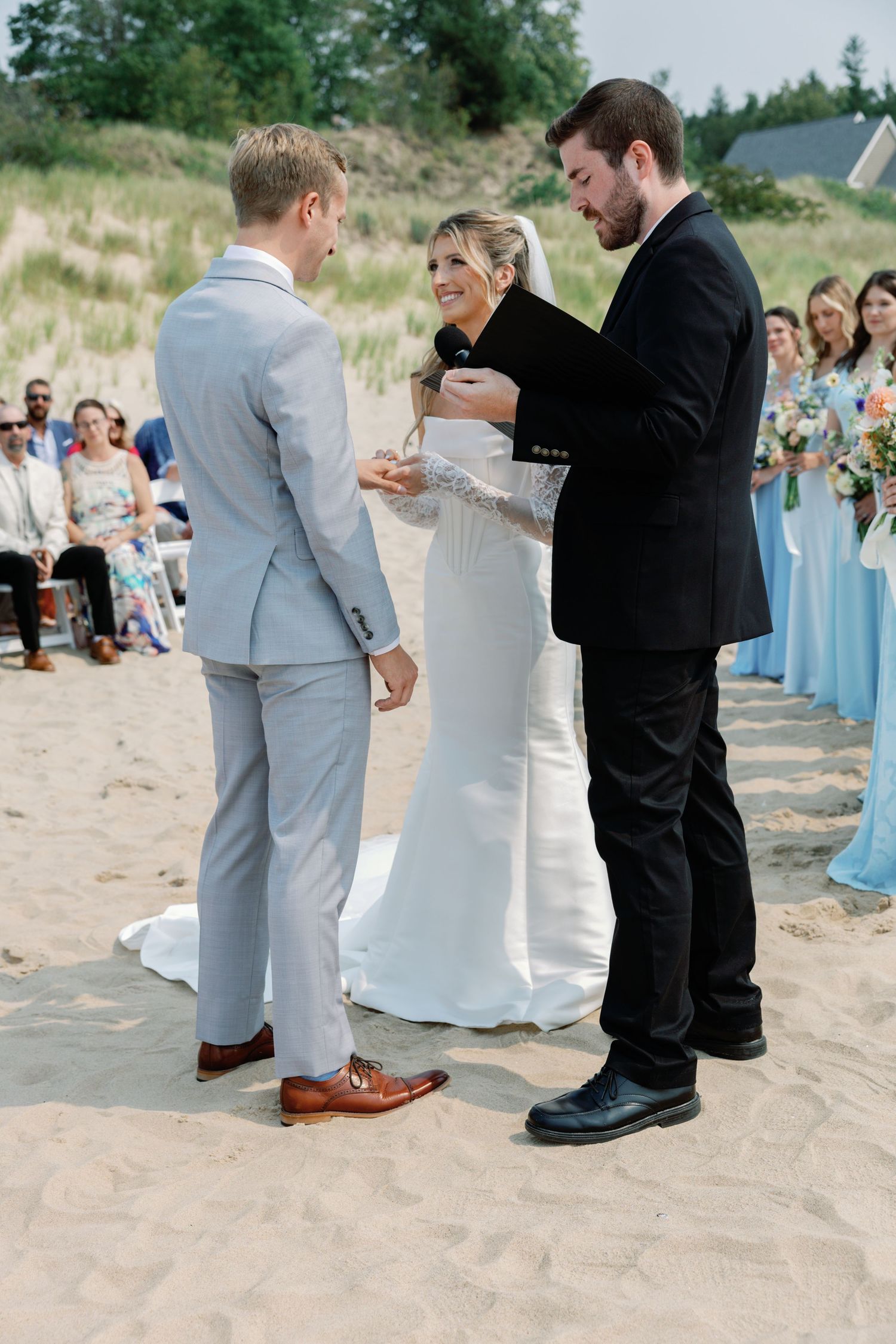Wedding ceremony details showing feet and lower legs of wedding party on beach sand.