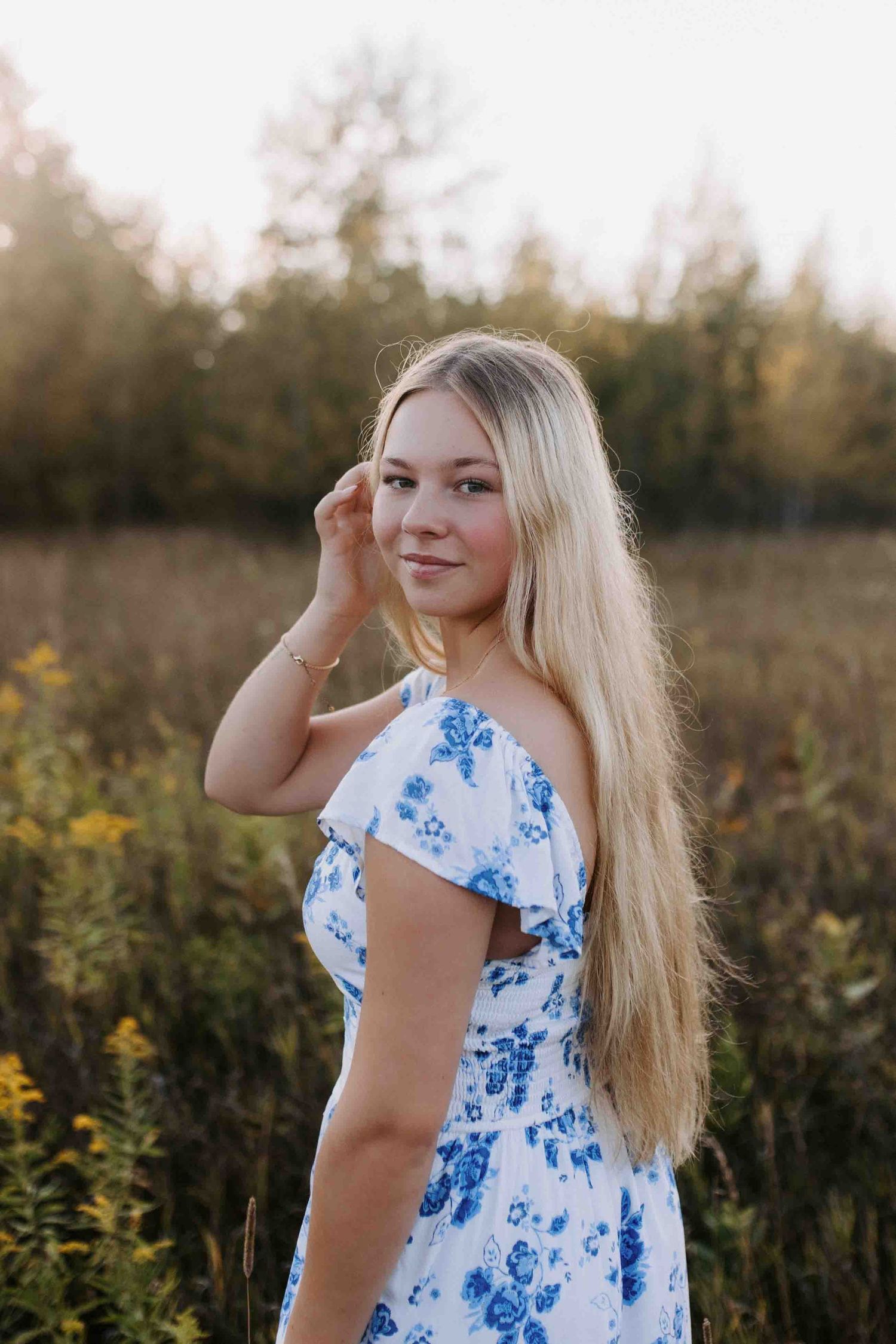 Blue and white floral dress captured in golden hour light among tall grass and wildflowers.