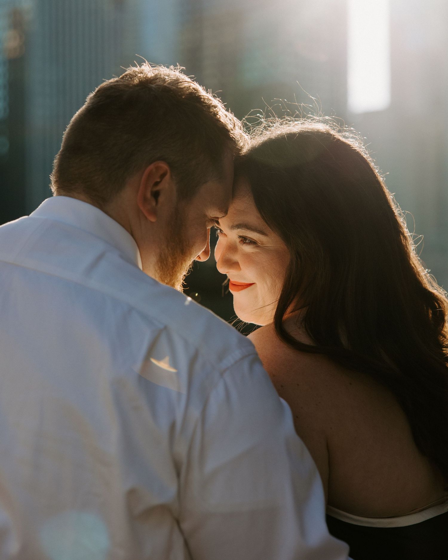 Romantic sunlit portrait of a couple sharing an intimate moment against an urban backdrop.