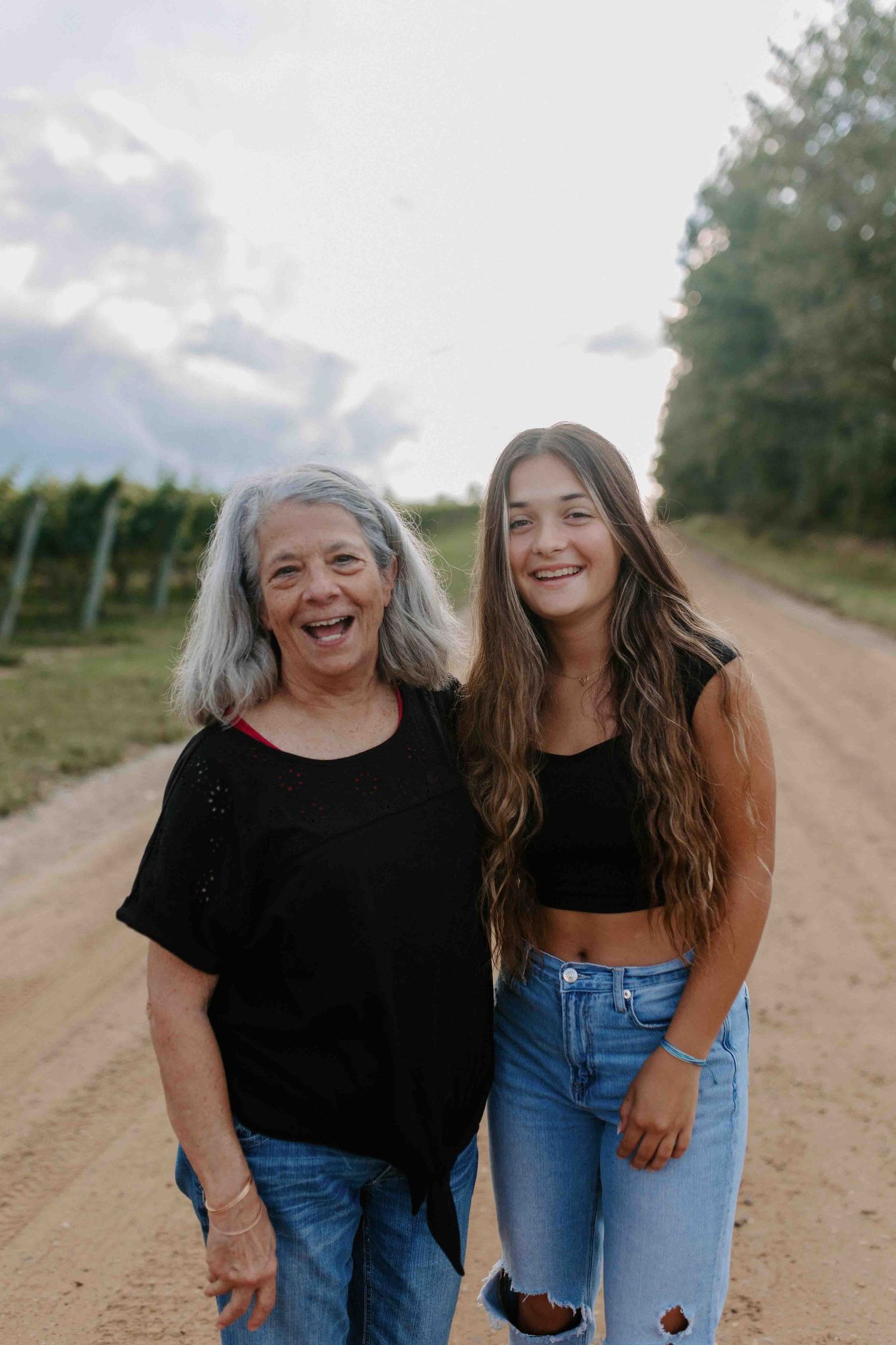 Two people share joyful laughter on a dirt road during a casual outdoor photoshoot.
