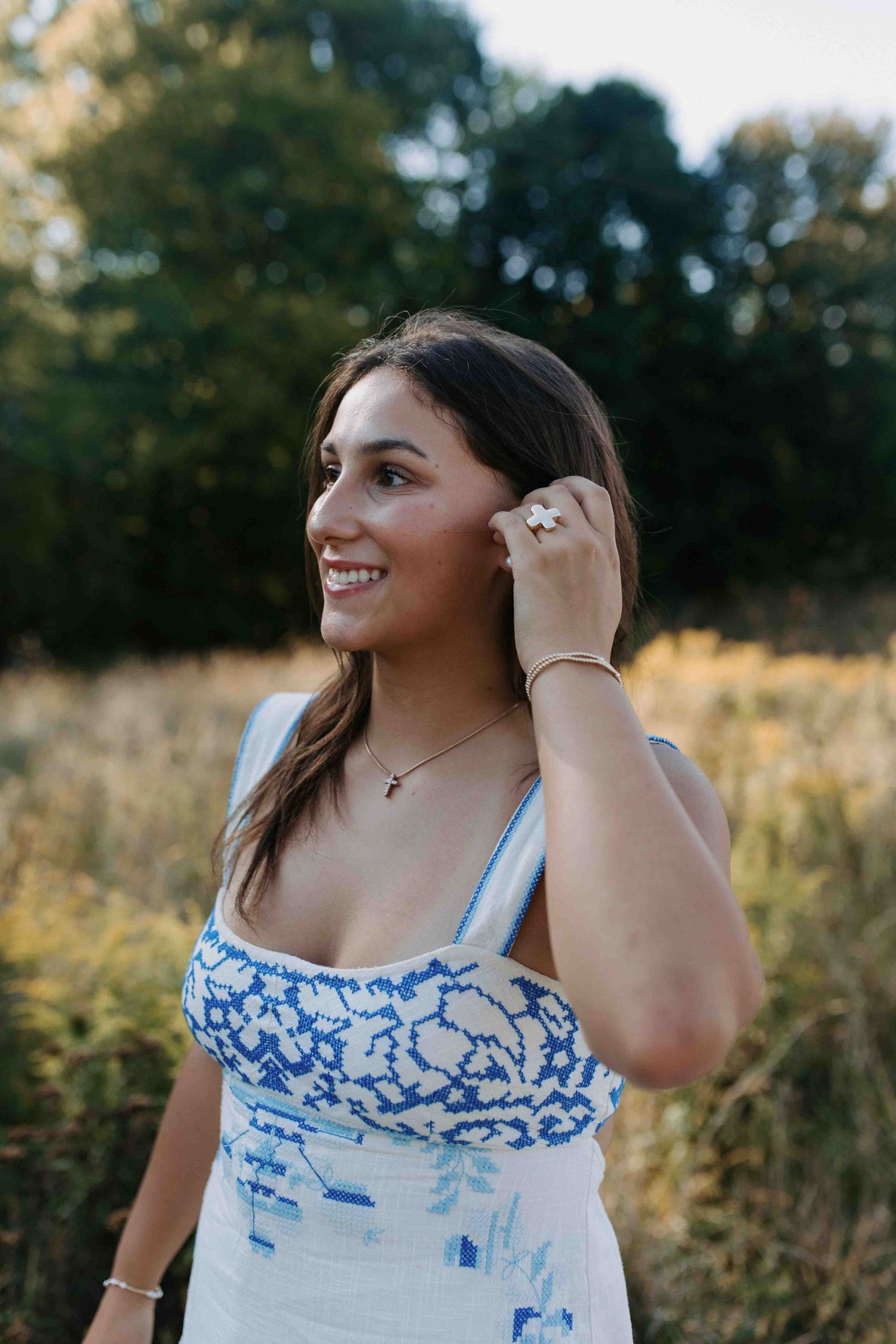 Portrait of someone wearing a white and blue patterned tank top in a sunny outdoor field at golden hour.