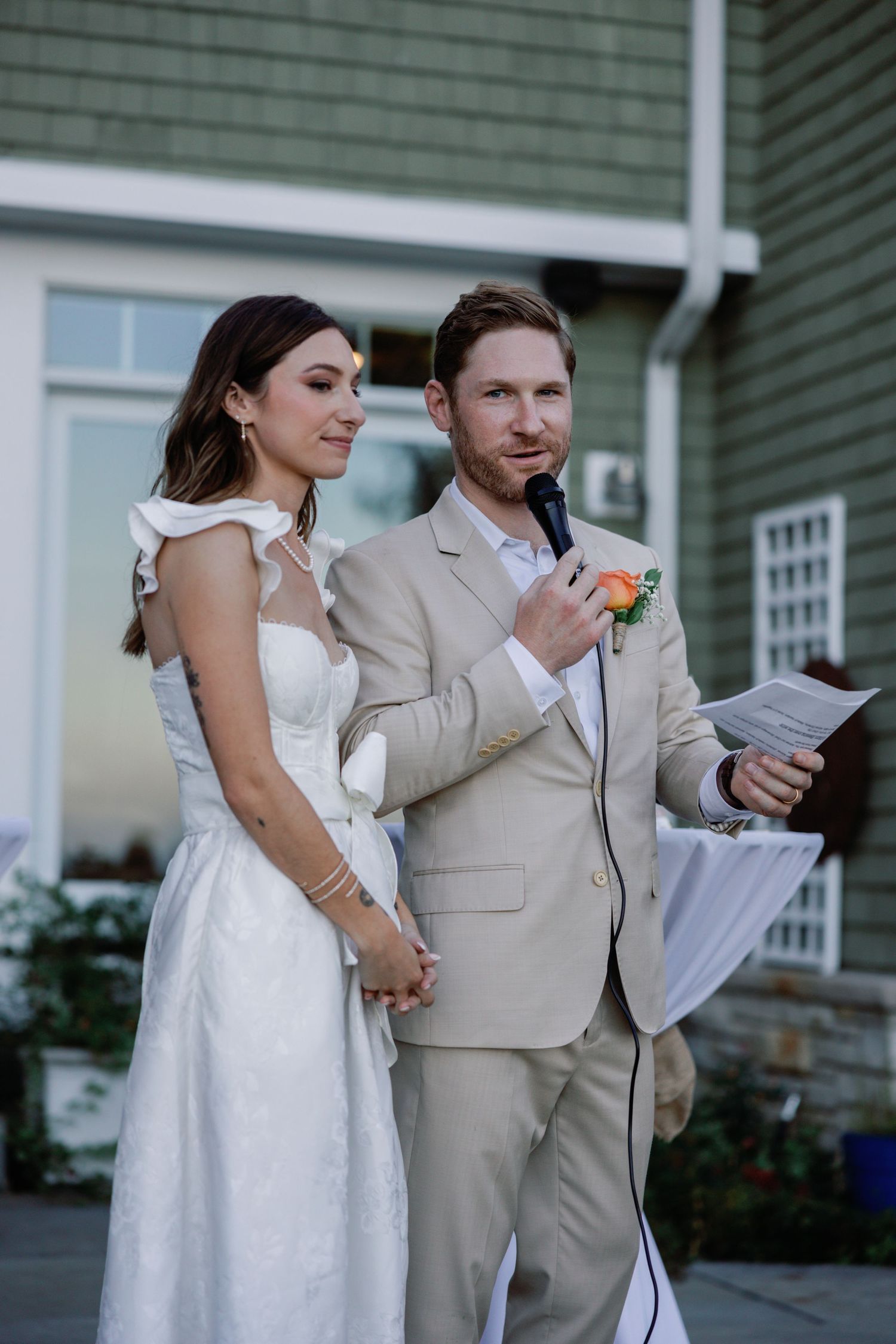 Wedding couple shares an intimate moment while walking together in formal attire outside a green building.