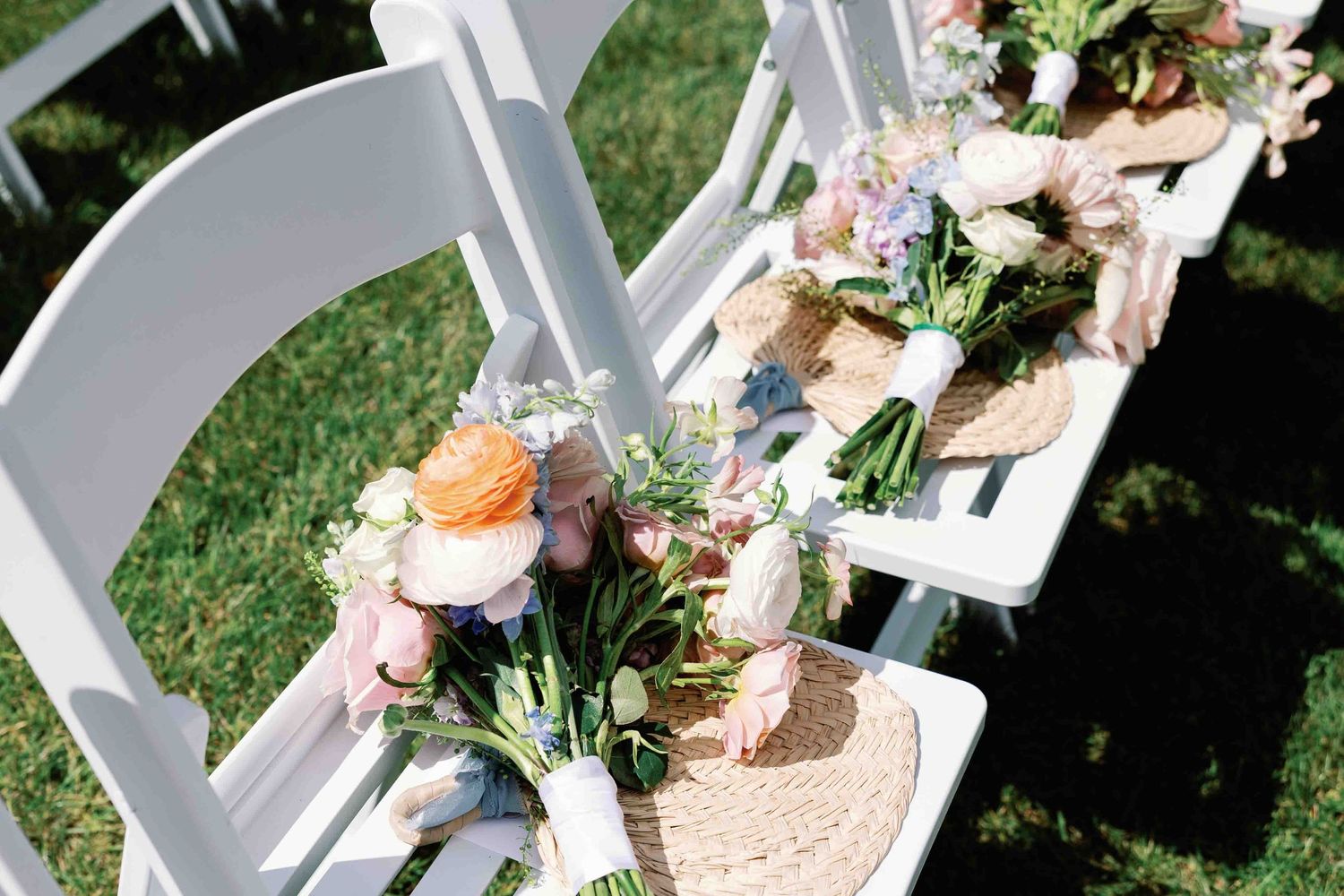 White folding chairs decorated with floral arrangements and burlap accents line up for an outdoor wedding ceremony.