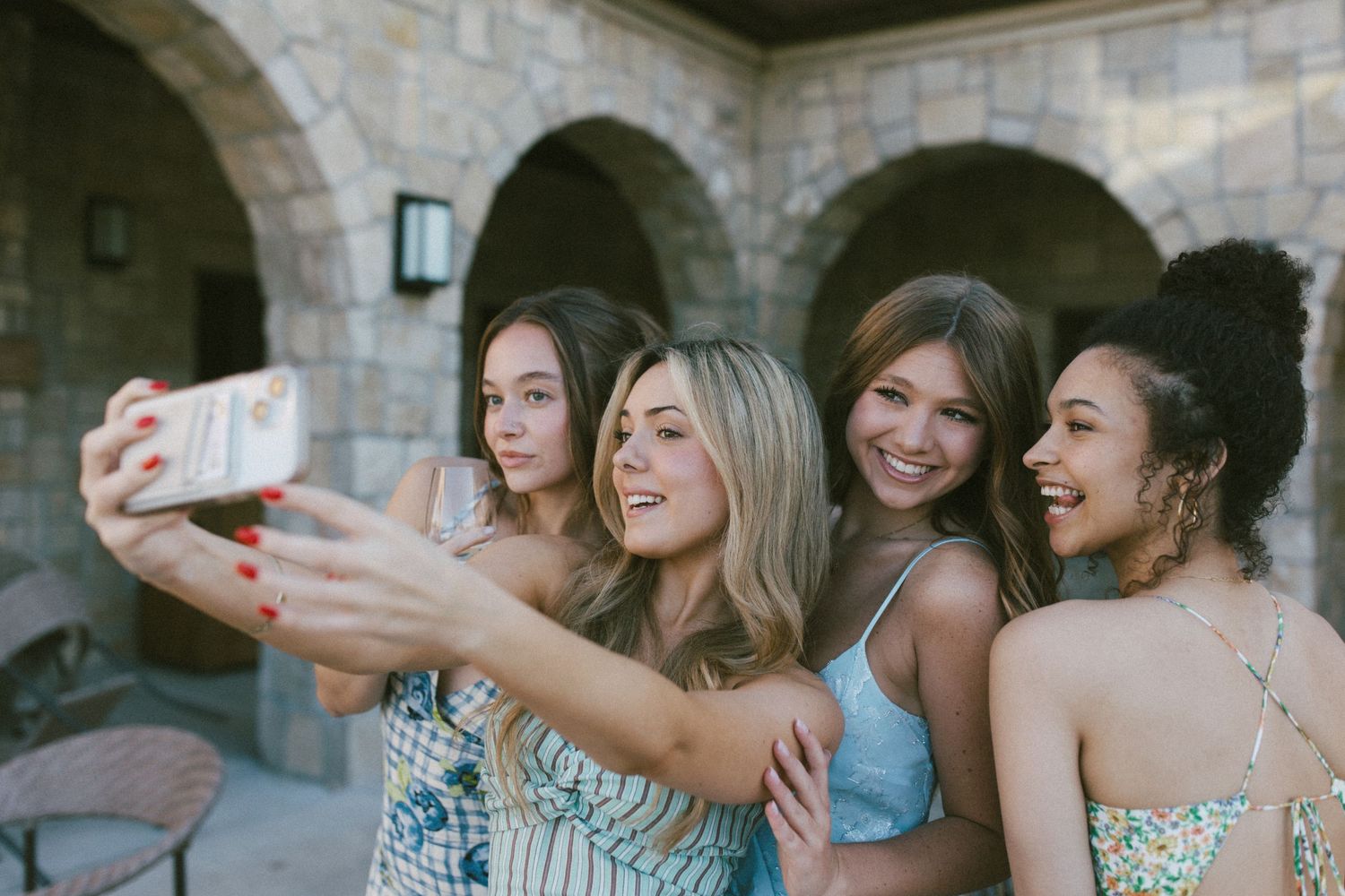 A group of friends in matching dresses taking selfies and celebrating together at an outdoor event.