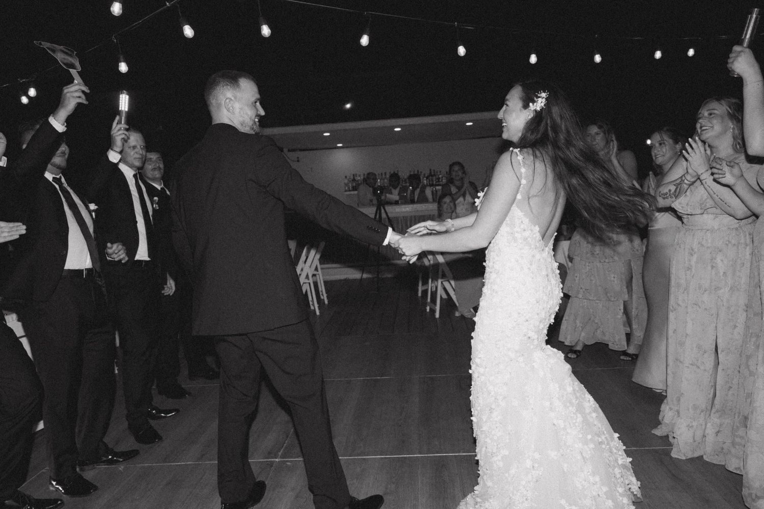 A couple shares their first dance at a wedding reception with string lights overhead.