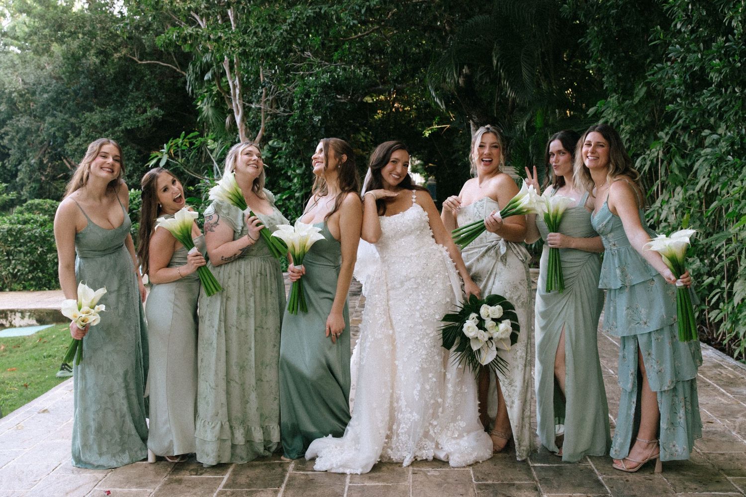 Wedding party in sage green dresses posing casually on garden lawn.
