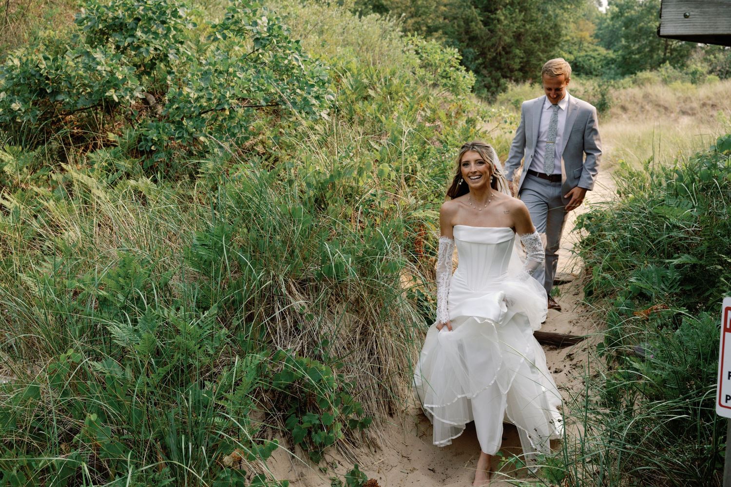 Wedding couple walks through a green garden path surrounded by lush vegetation.
