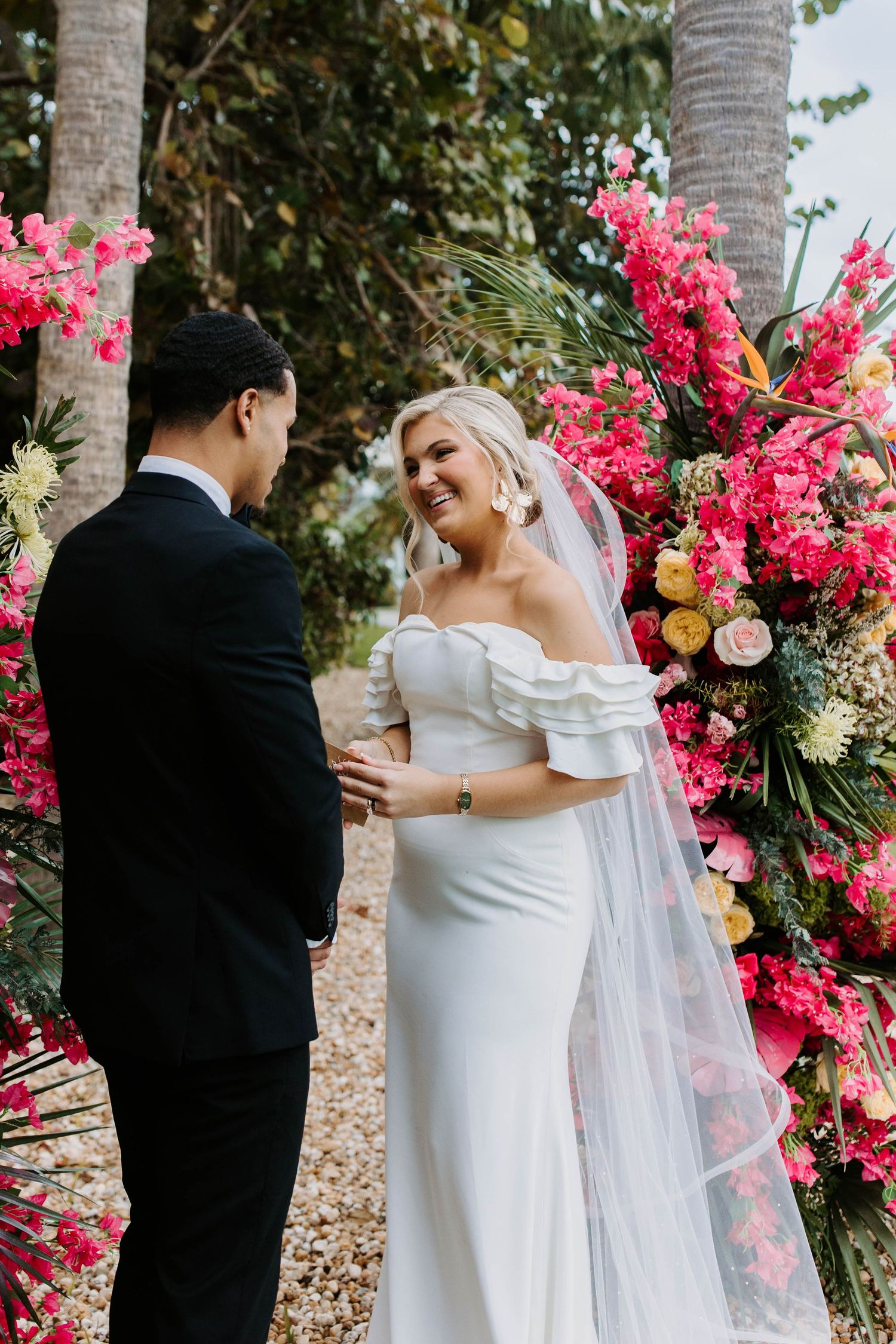 Elegant wedding portraits framed by tropical palm trees and bright pink floral arrangements.