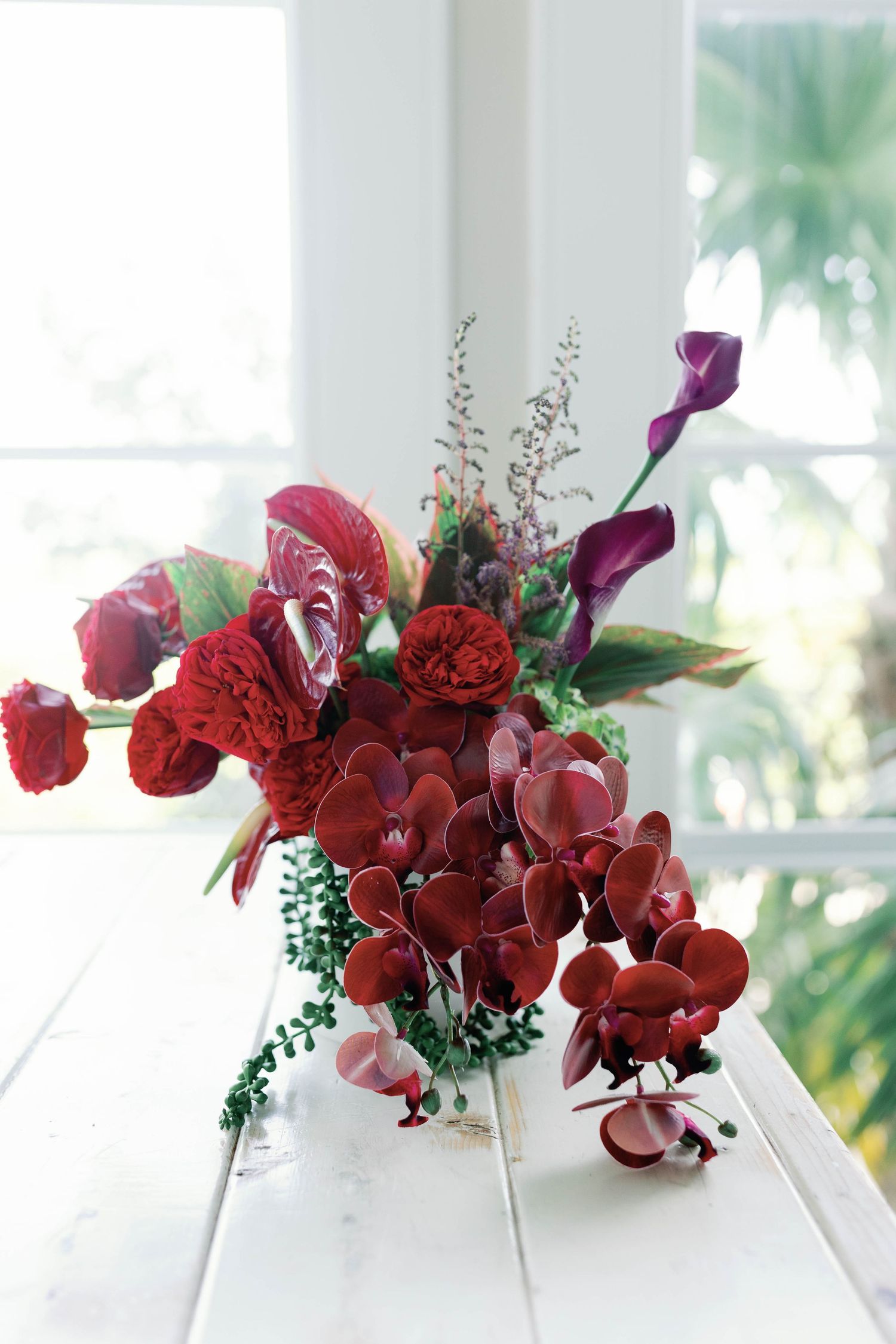 Elegant red floral arrangement with orchids and roses displayed on white surface.