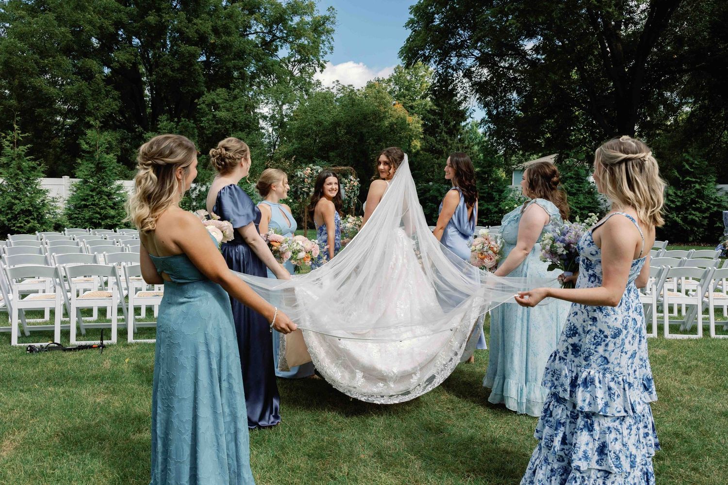 Wedding party poses and celebrates on a lawn with white chairs visible in the background.