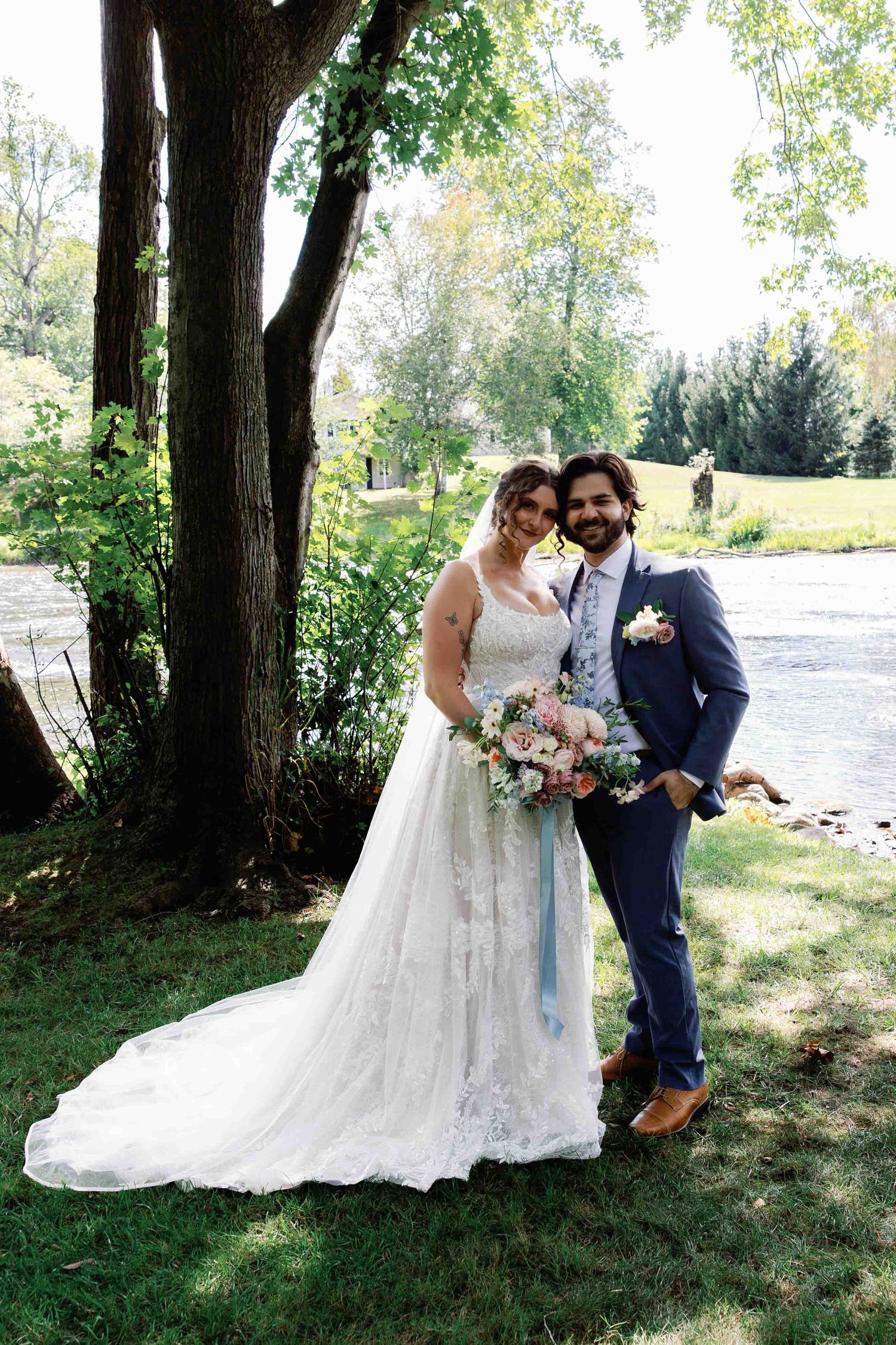 A couple shares an intimate moment by a riverside on their wedding day surrounded by lush greenery.