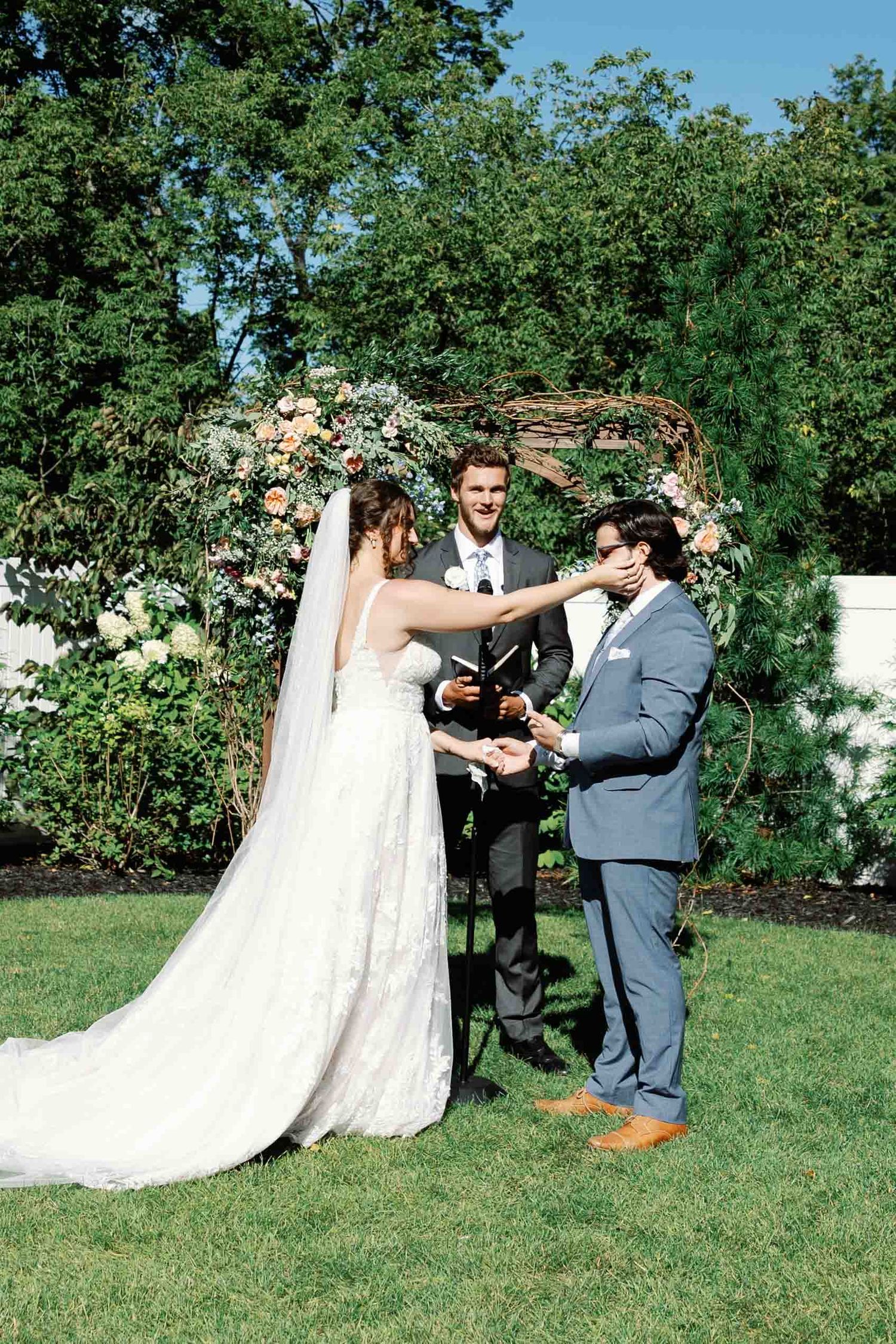 Couple shares a playful moment during their outdoor wedding ceremony on a grassy lawn.