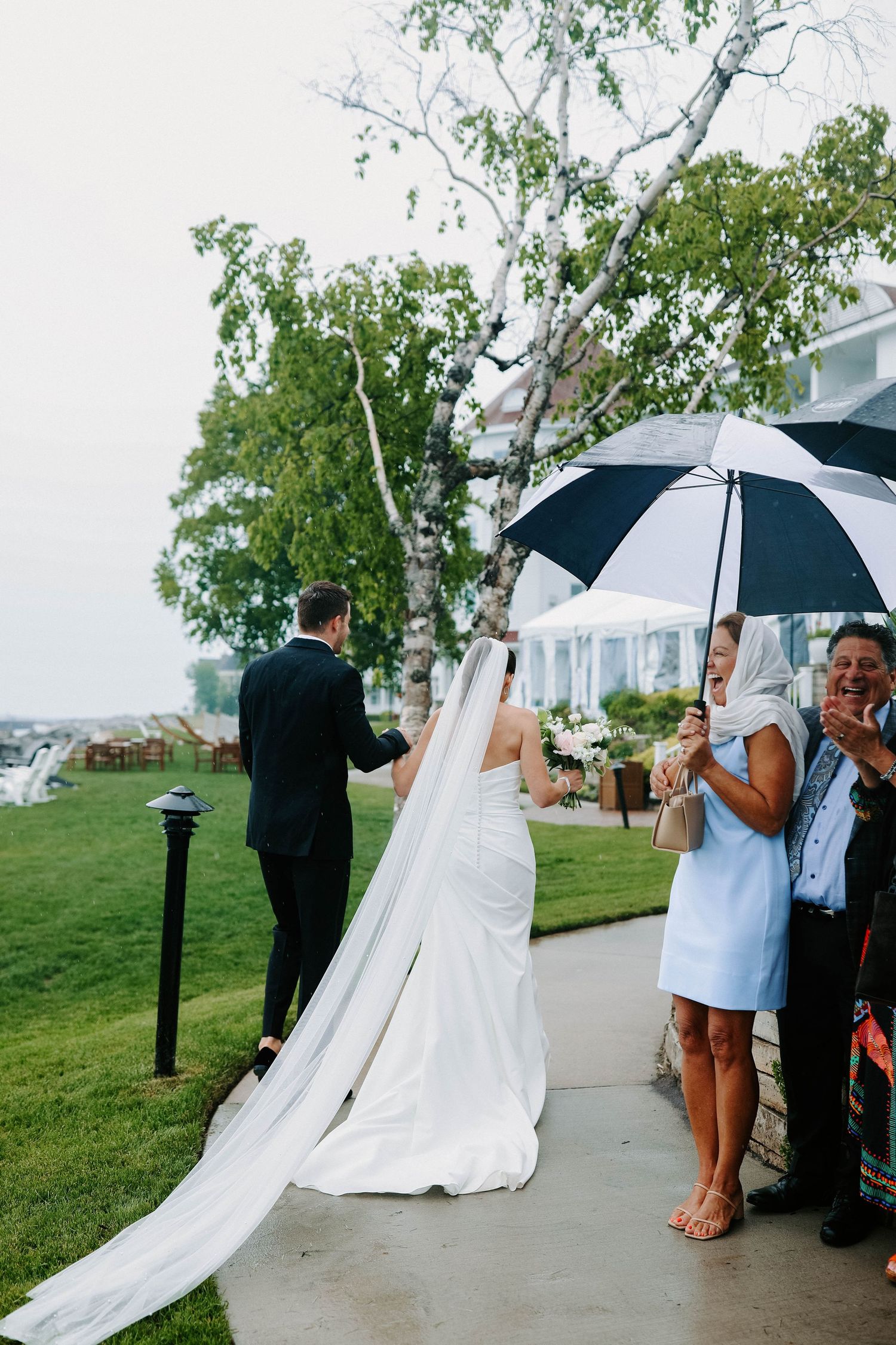 Wedding guests with umbrellas gather on a grassy hill during a rainy outdoor ceremony.