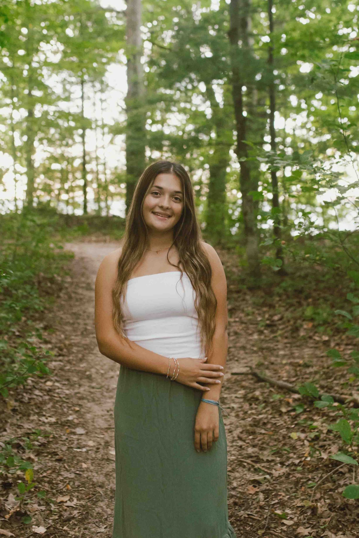 A peaceful forest scene with a white tank top and sage green skirt outfit against natural foliage.