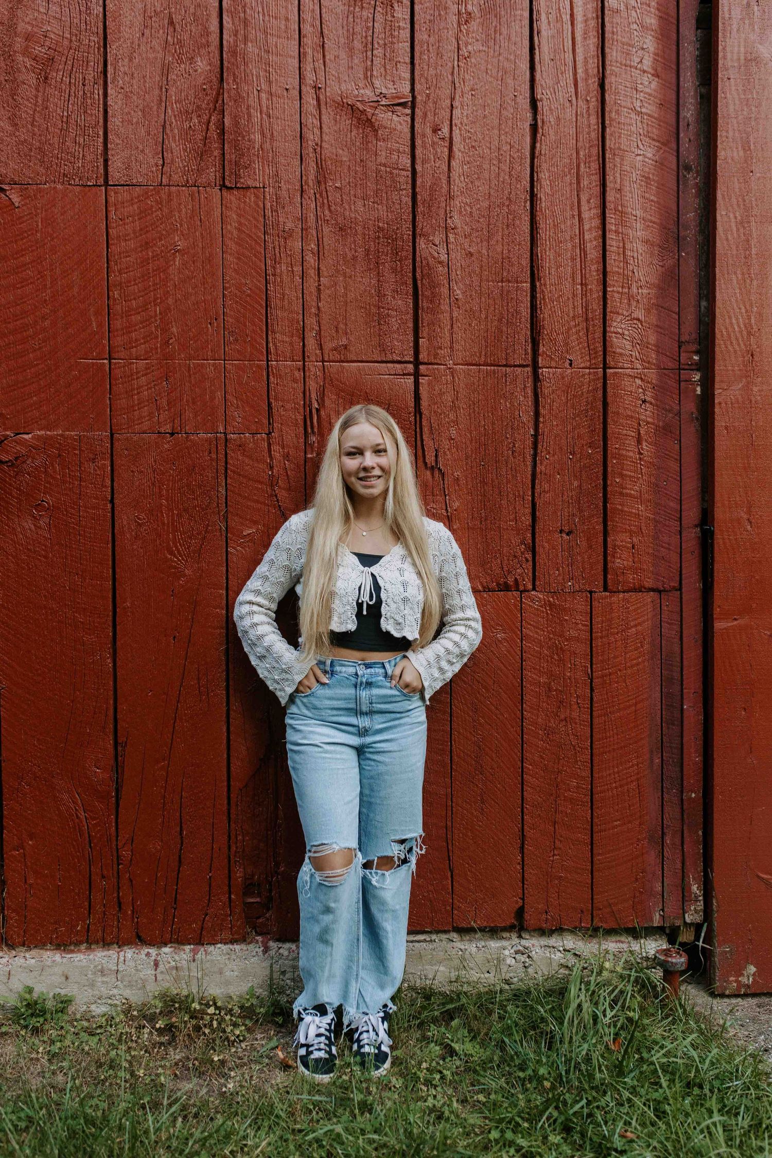 Casual outfit with ripped jeans and sneakers against rustic red barn wall.