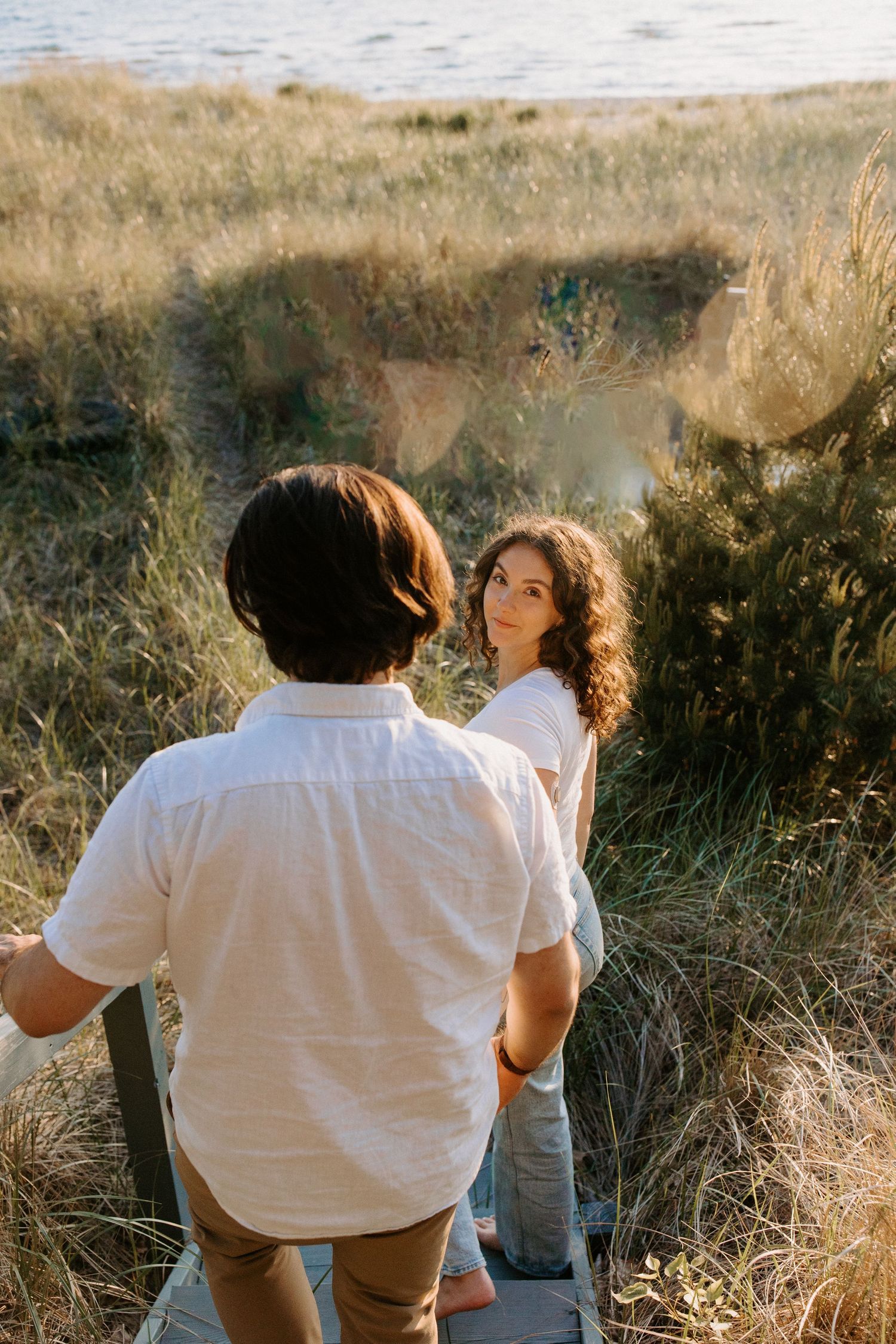 Couple sharing an intimate moment in coastal grass during sunset.