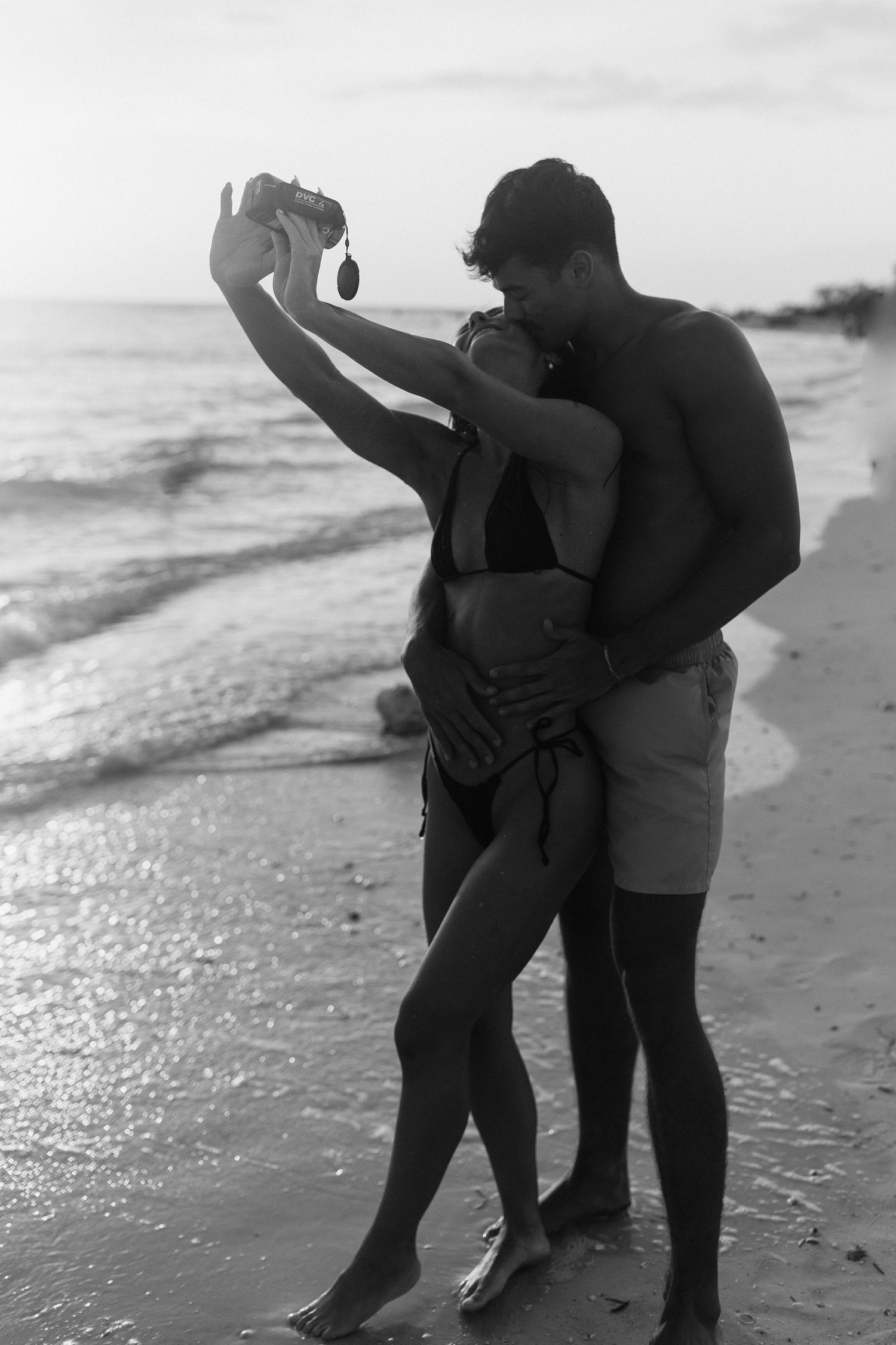Couple dancing together on a sunlit beach with waves in the background.