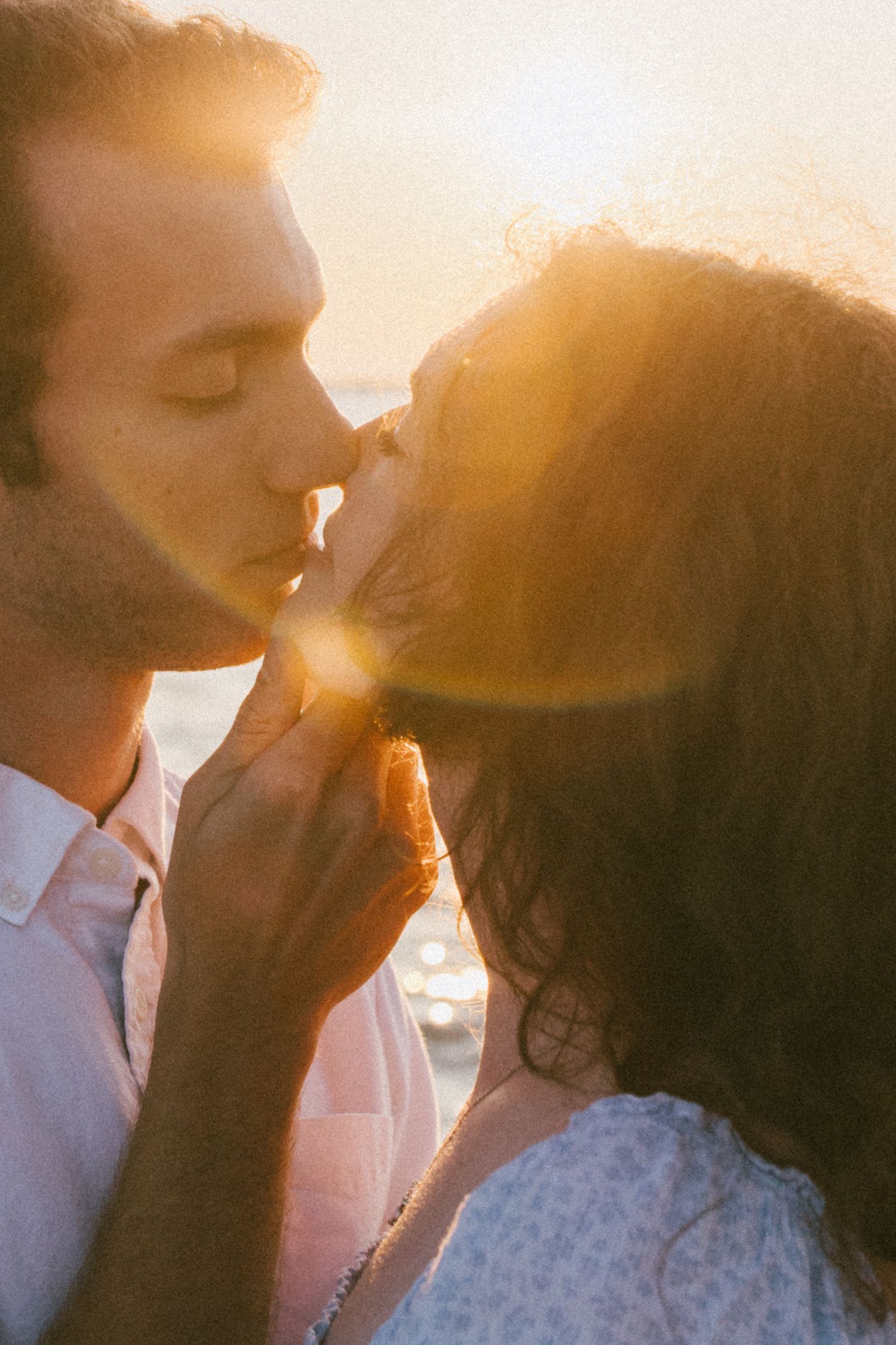 Silhouetted couple kissing during golden hour with sun flare.