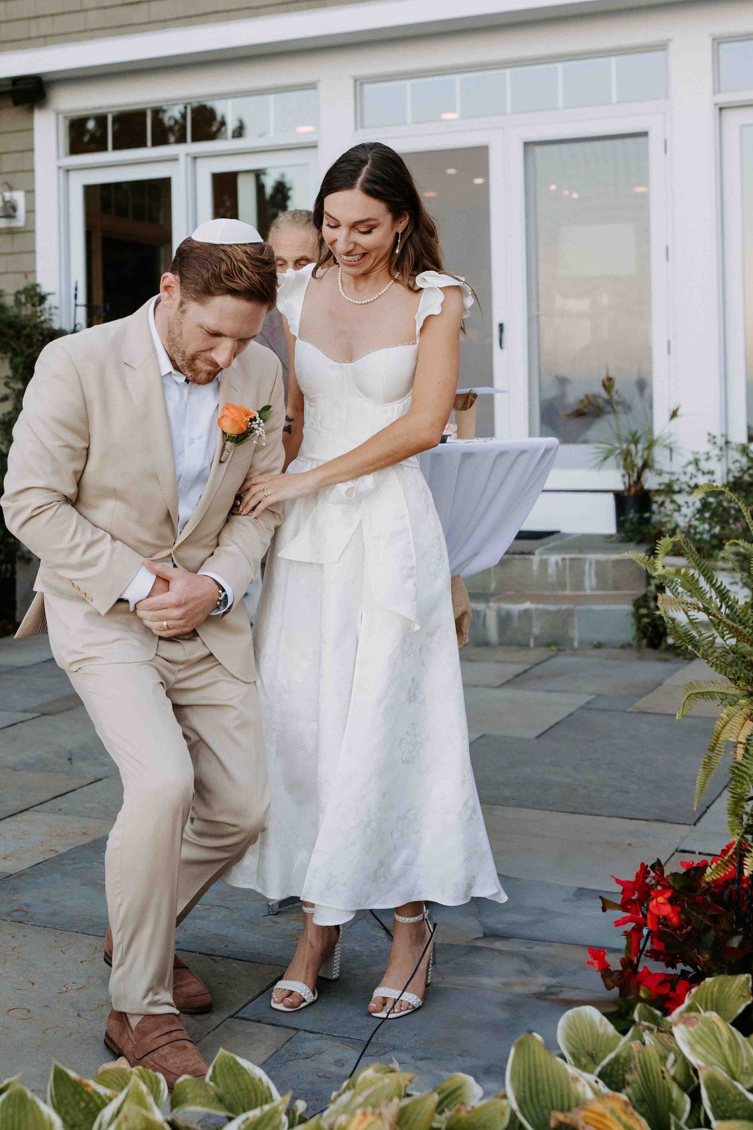 Couple sharing playful moment near garden planters in wedding attire.