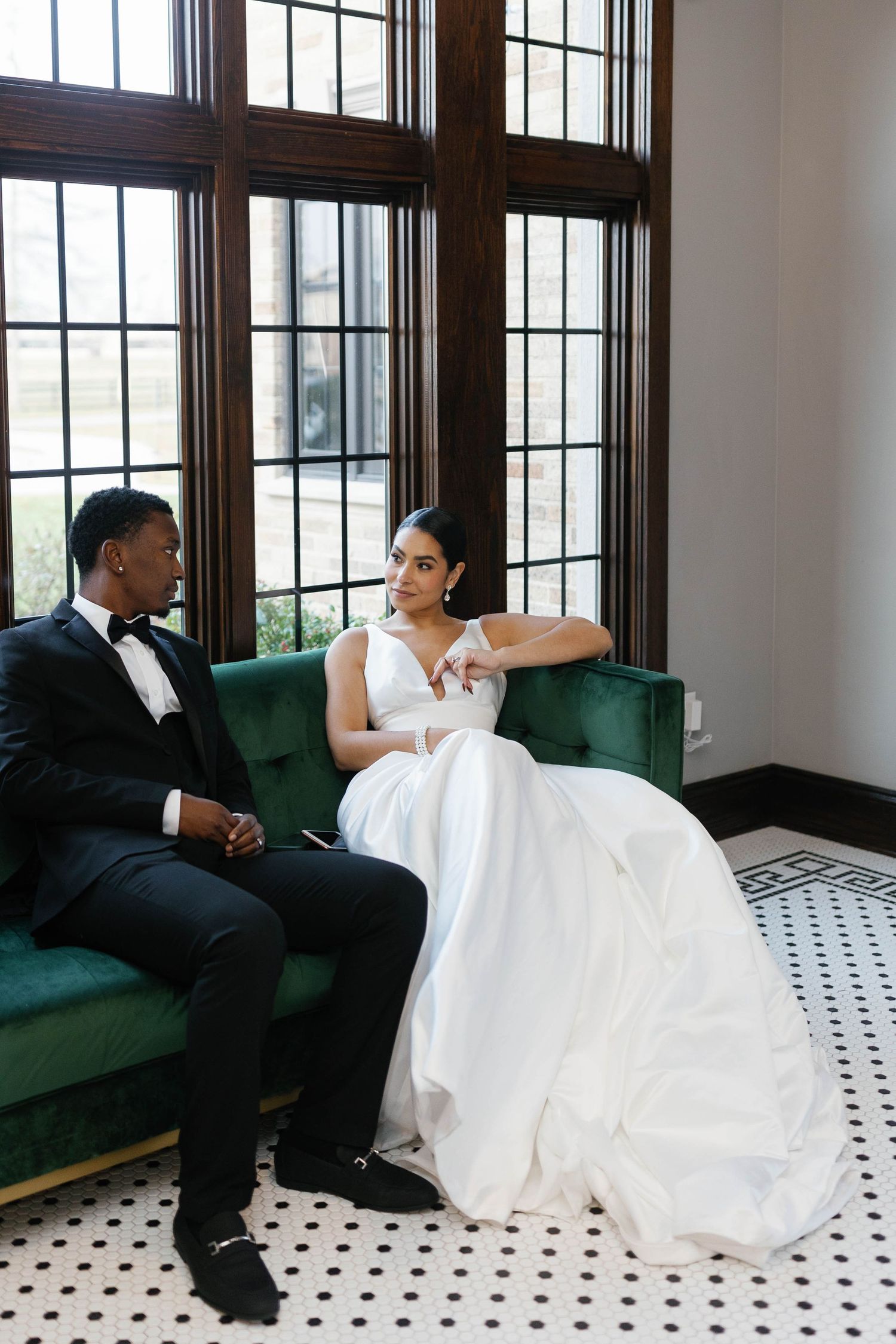Elegant wedding couple posing on green velvet couch in a room with checkered floors.