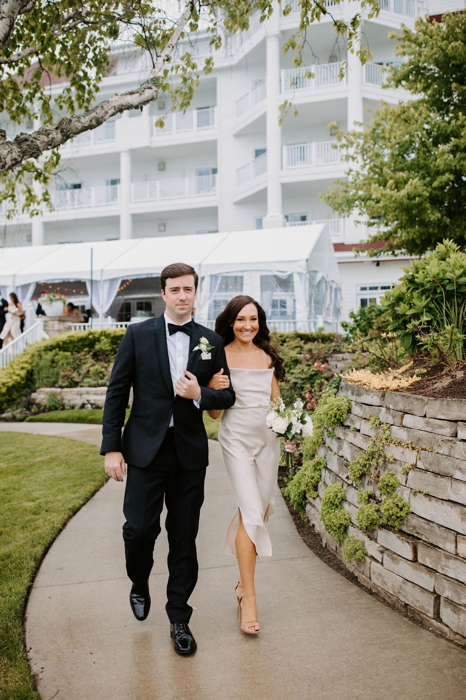 Wedding party members walk along a curved pathway beside a white resort building.