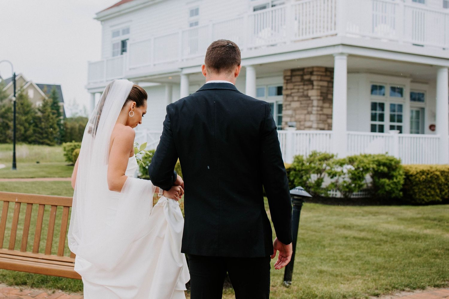 Wedding couple walking along pathway near white coastal building with ocean views.