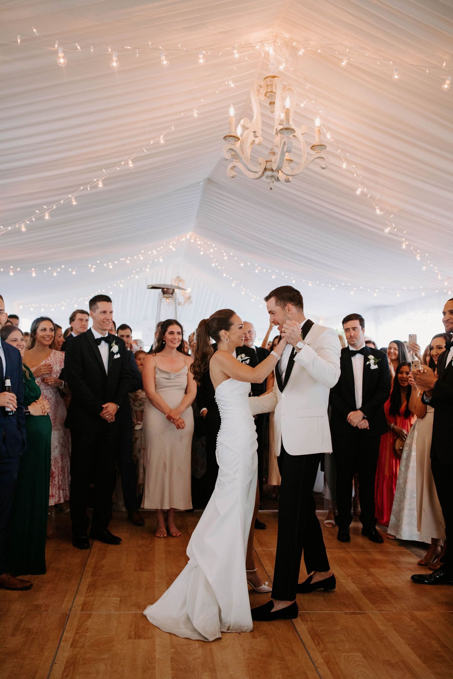 Couples dancing at an elegant tented wedding reception with string lights and chandeliers.