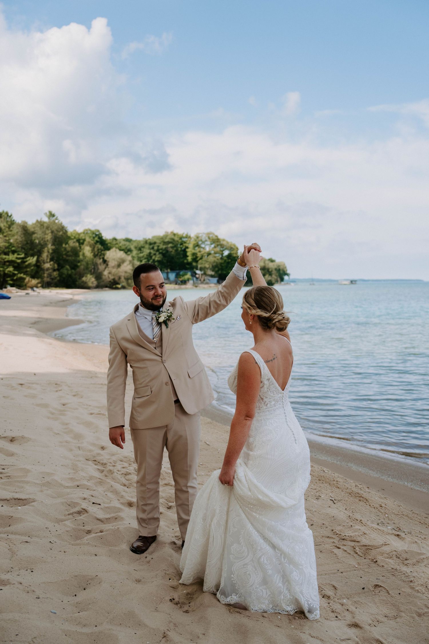 Newlyweds in formal attire dance and celebrate together on a scenic beach.