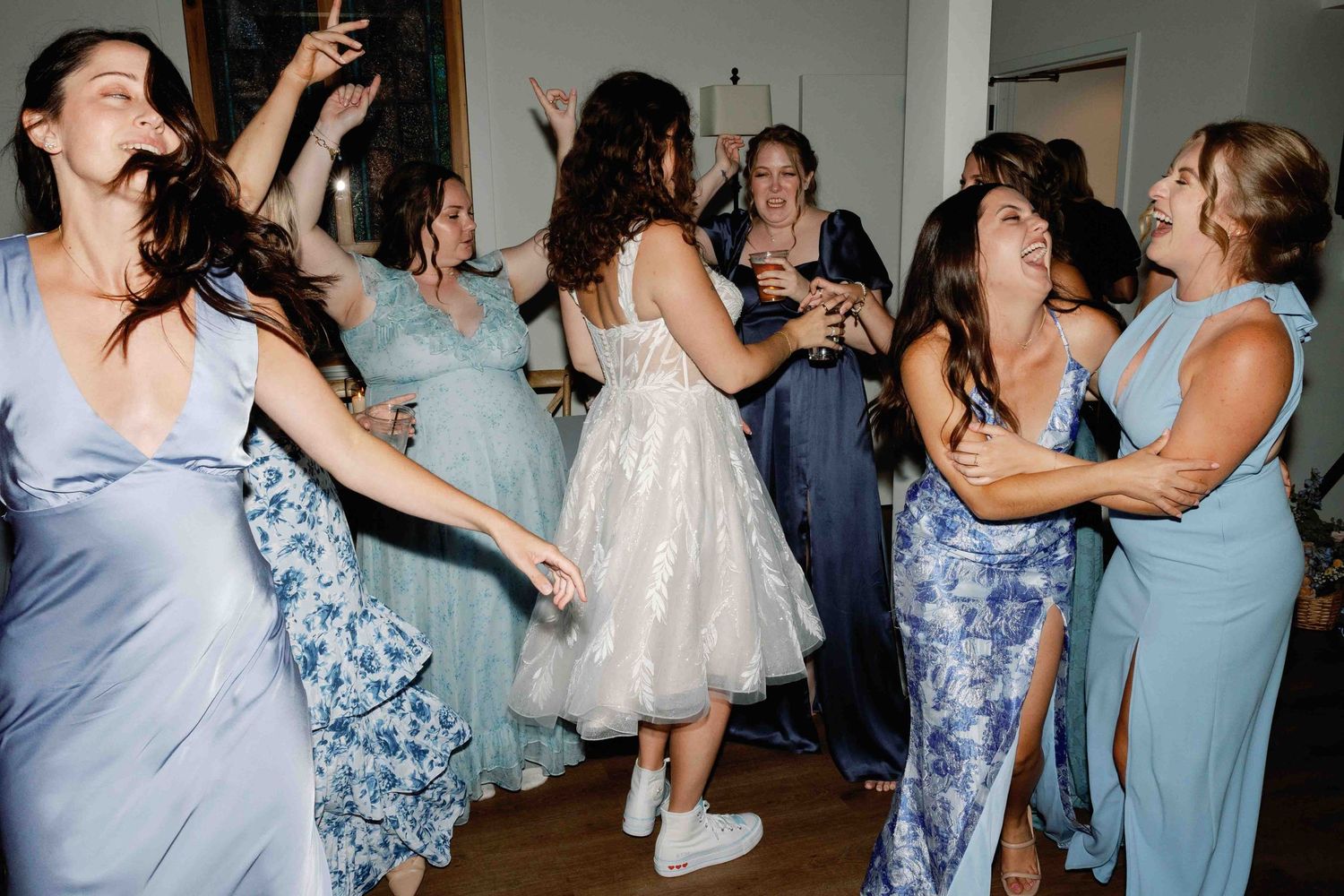 Wedding party dancing and celebrating in coordinated blue and floral dresses.