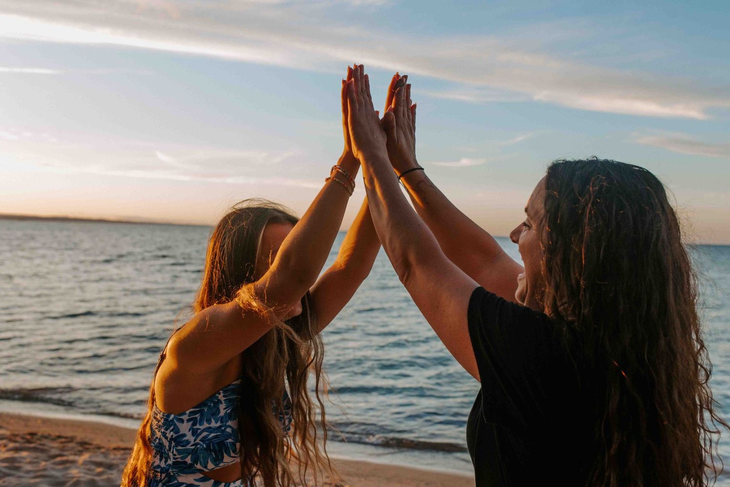 Two people dance and celebrate on a sandy beach during sunset.