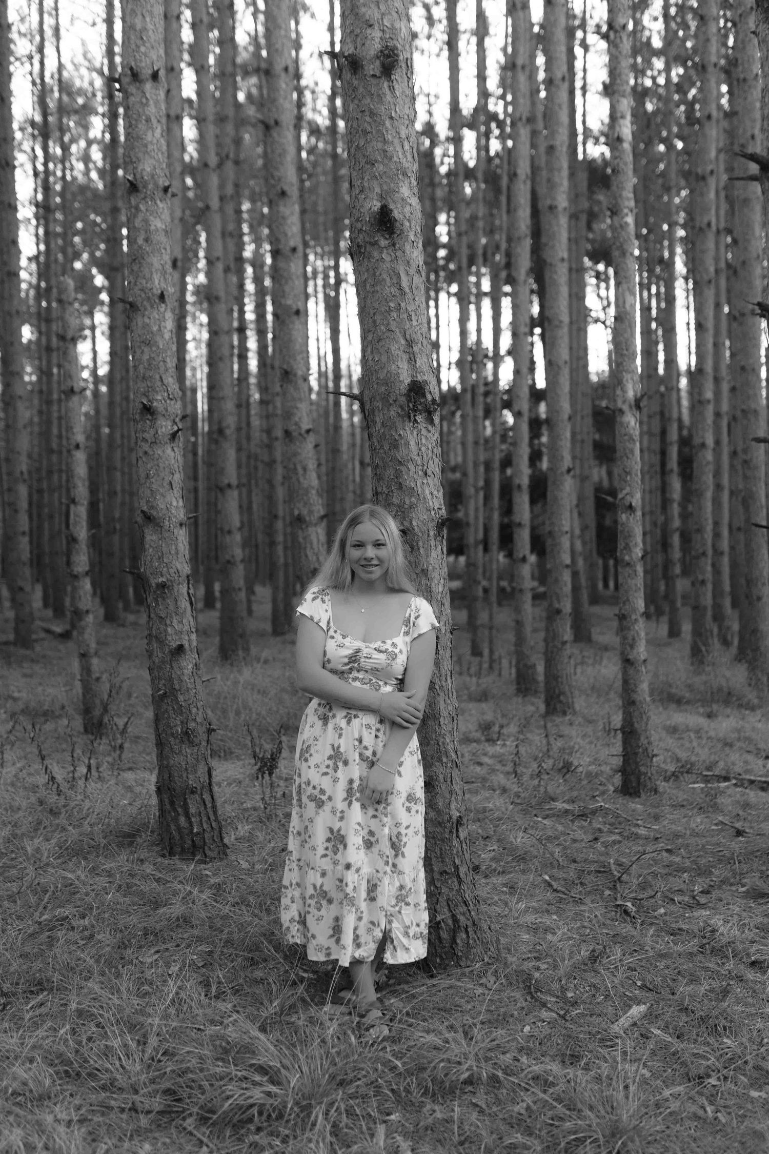 Black and white forest portrait showing a floral dress among tall pine trees.