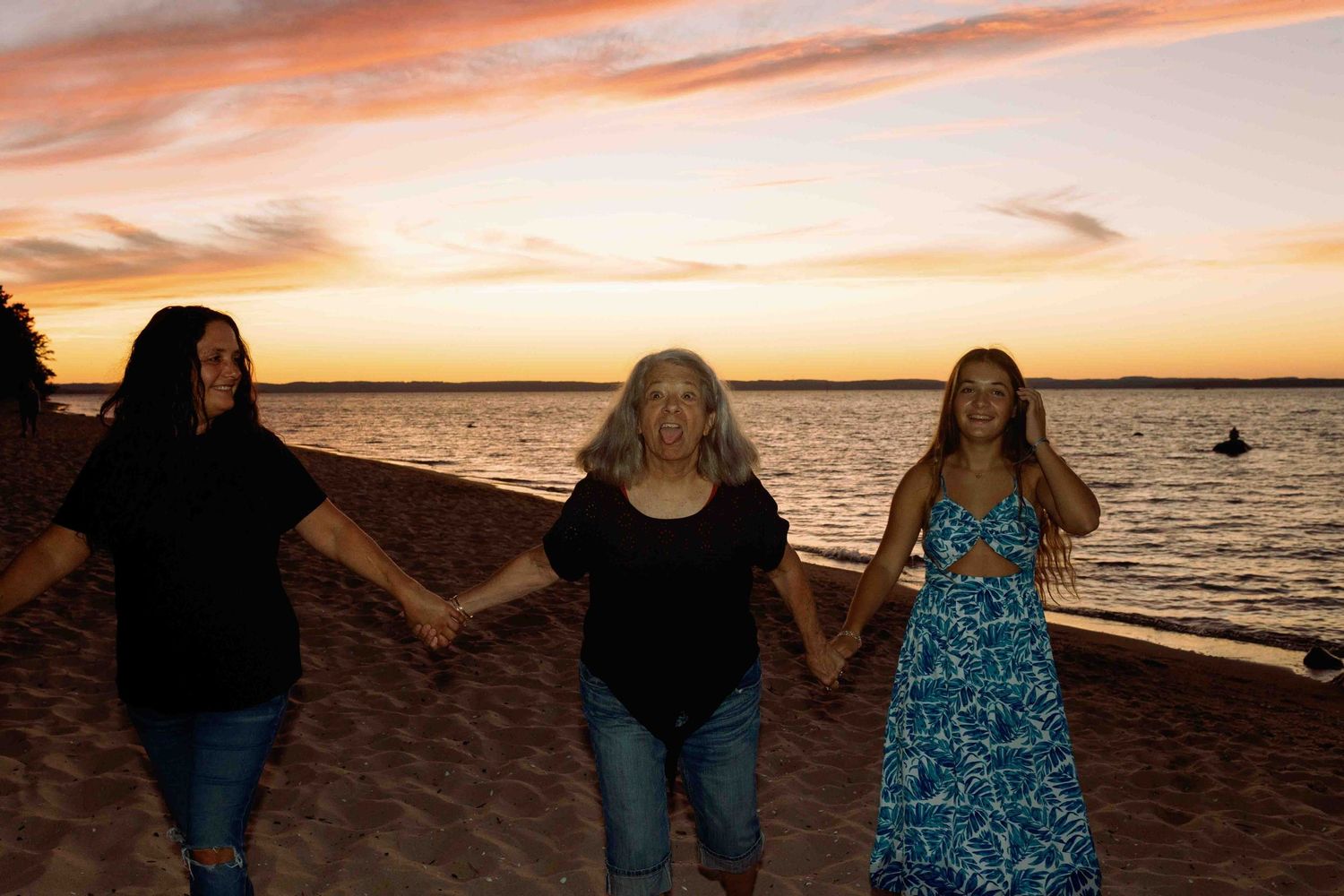 Group of people walking along beach shore during golden hour sunset.