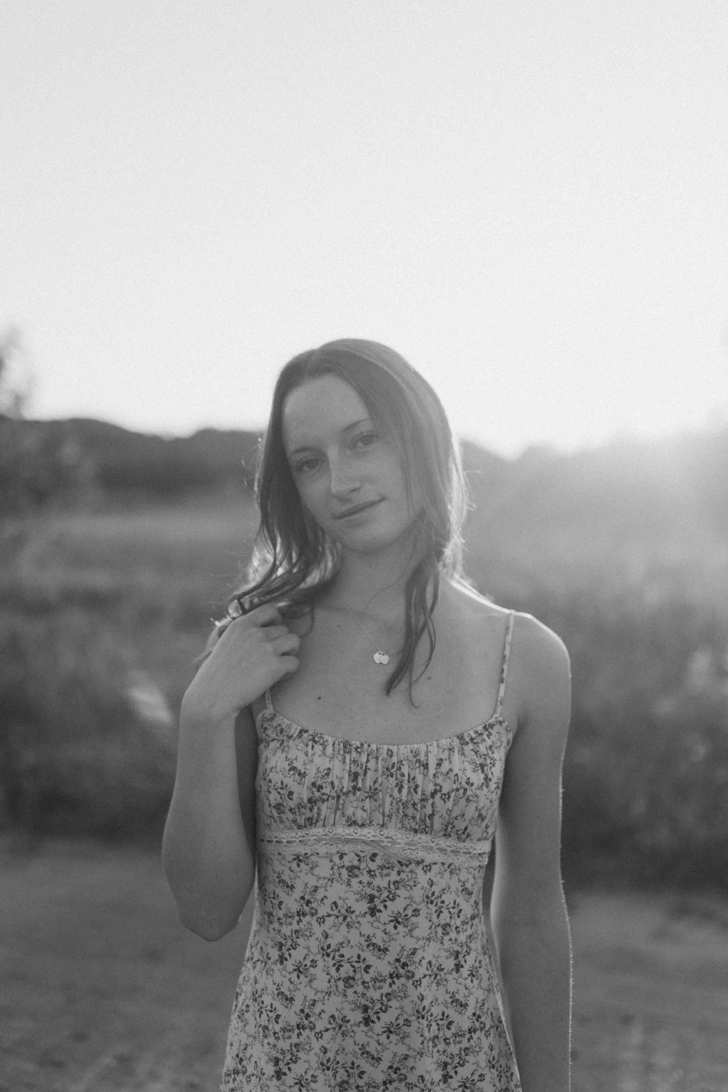 Black and white portrait capturing someone in natural light against a rural backdrop.