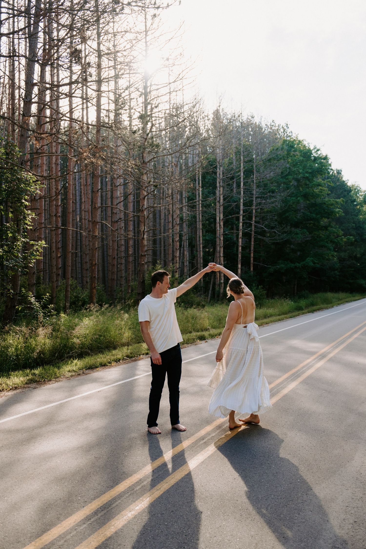 A couple dances and twirls together on an empty forest road during a sunny day.