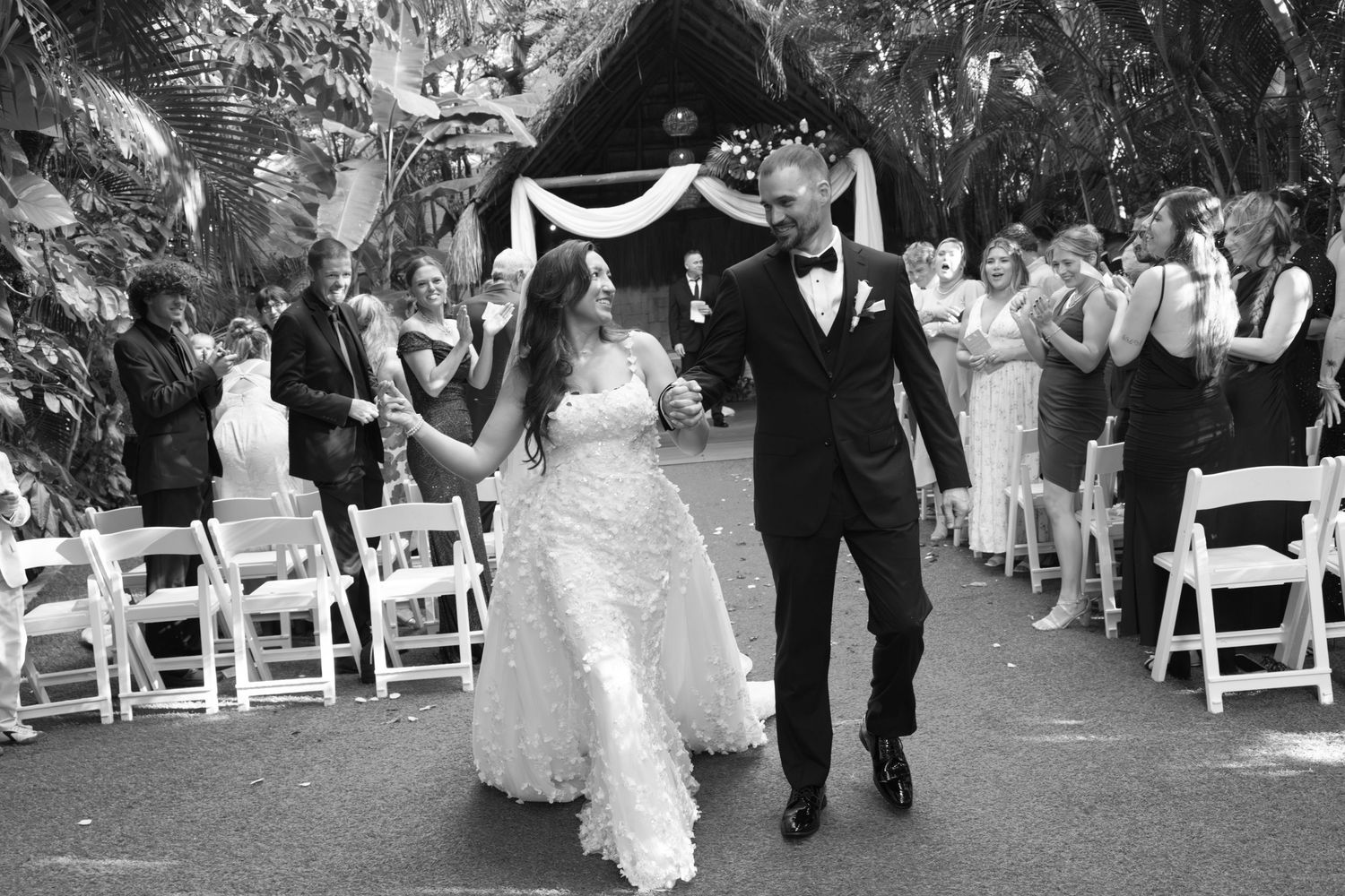 Wedding ceremony procession with white chairs and guests outdoors.