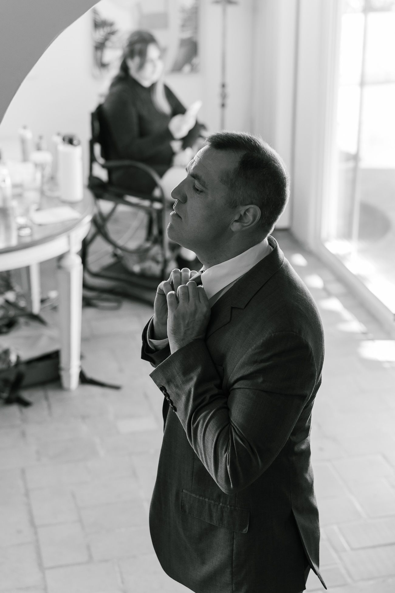 Black and white photo of groom adjusting tie while getting ready on wedding day.