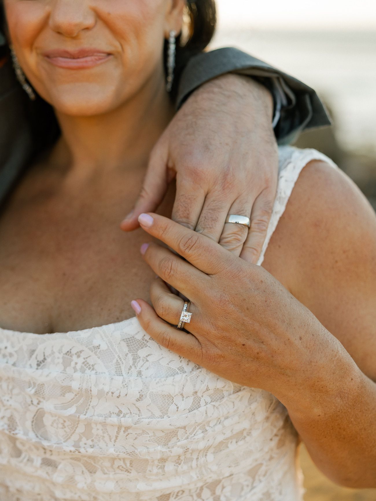 Close-up shot of hands showing off elegant wedding rings against a white lace dress.