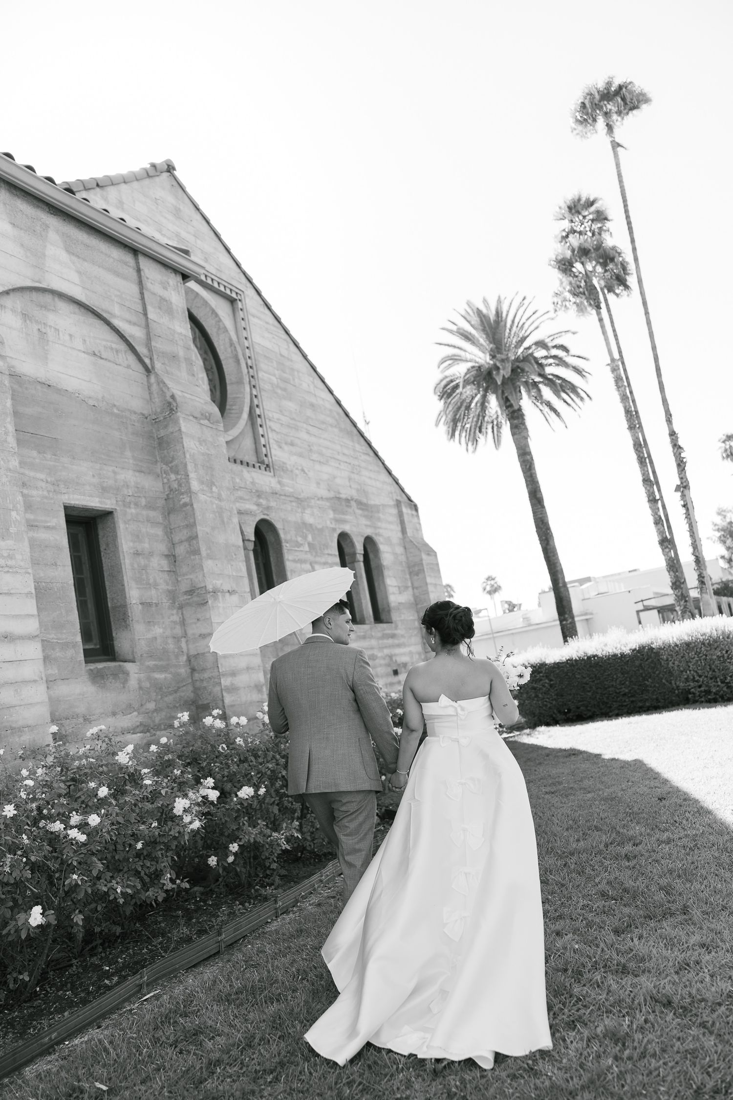 A romantic black and white photo outside a Spanish-style church with tall palm trees in the background.