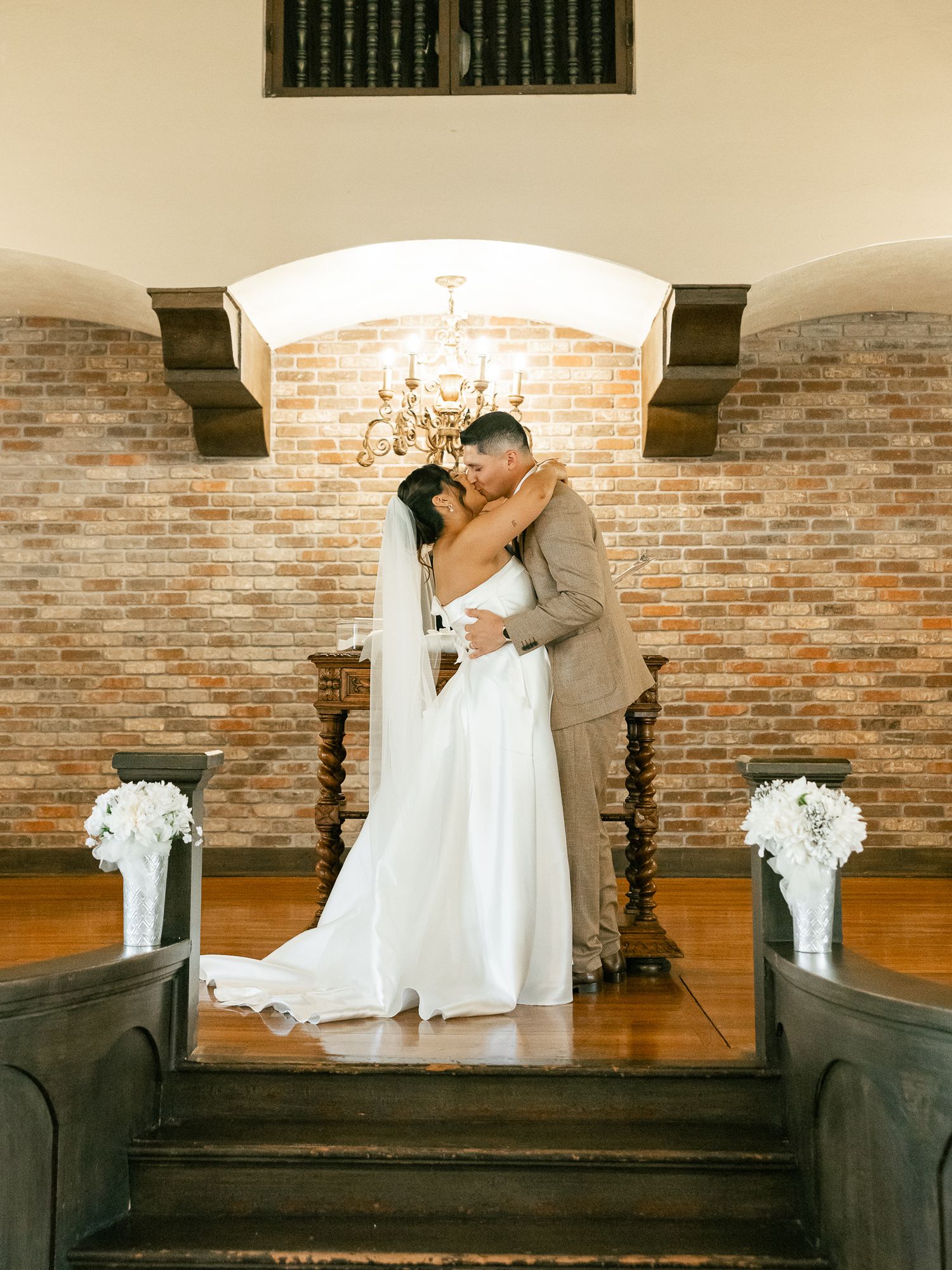 Wedding ceremony at rustic brick chapel with elegant chandelier and floral arrangements.
