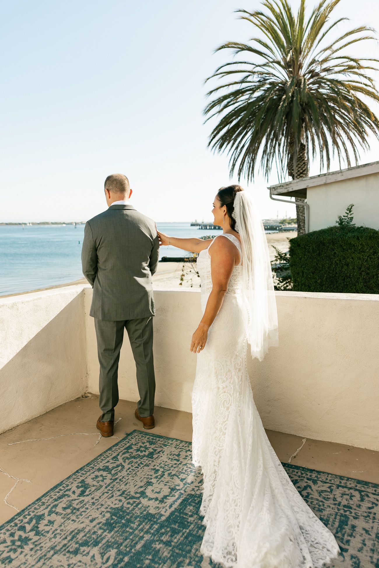 A couple shares a romantic moment on a coastal balcony with a palm tree and ocean view on their wedding day.