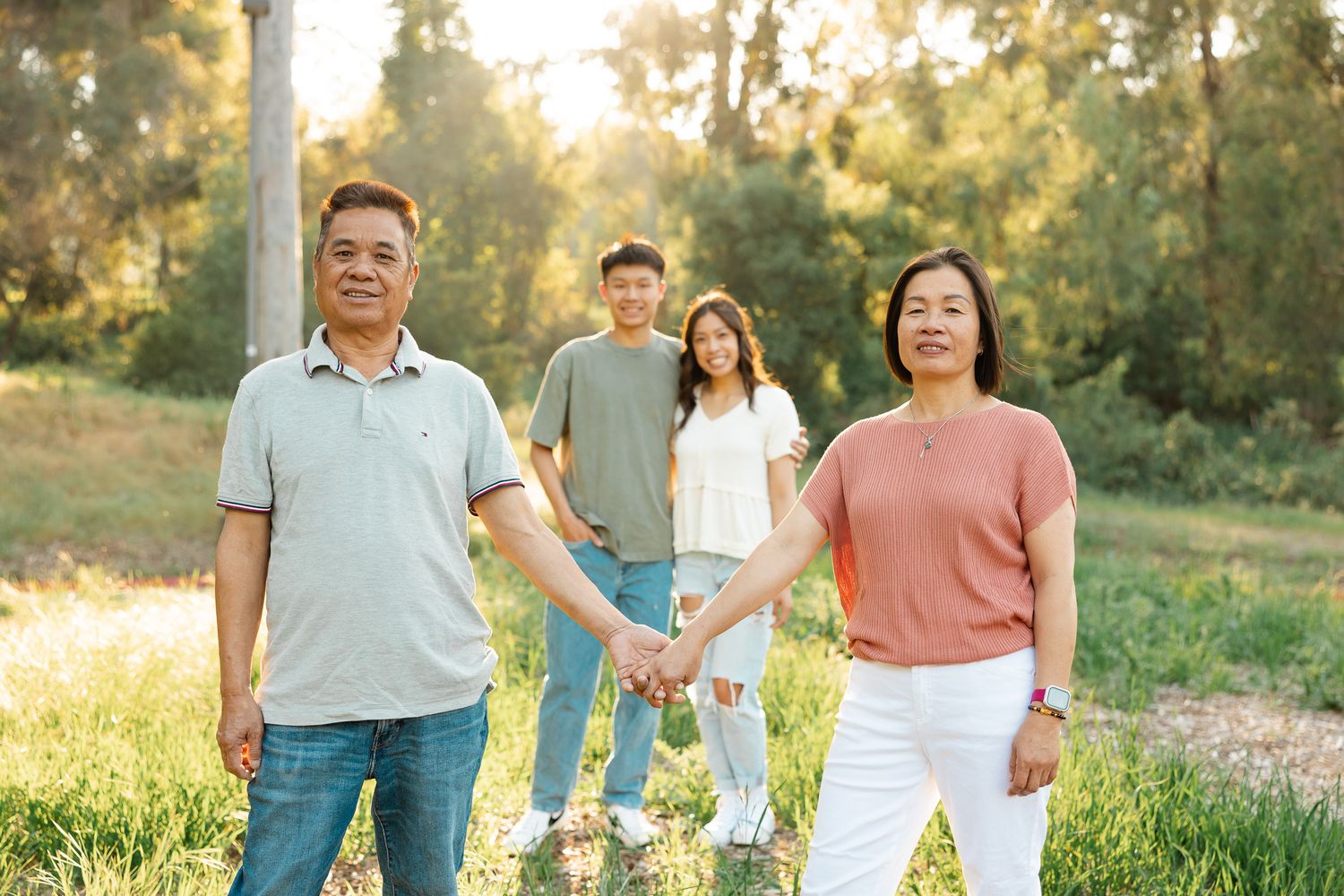 Asian family of four posing together outdoors during golden hour in casual attire.