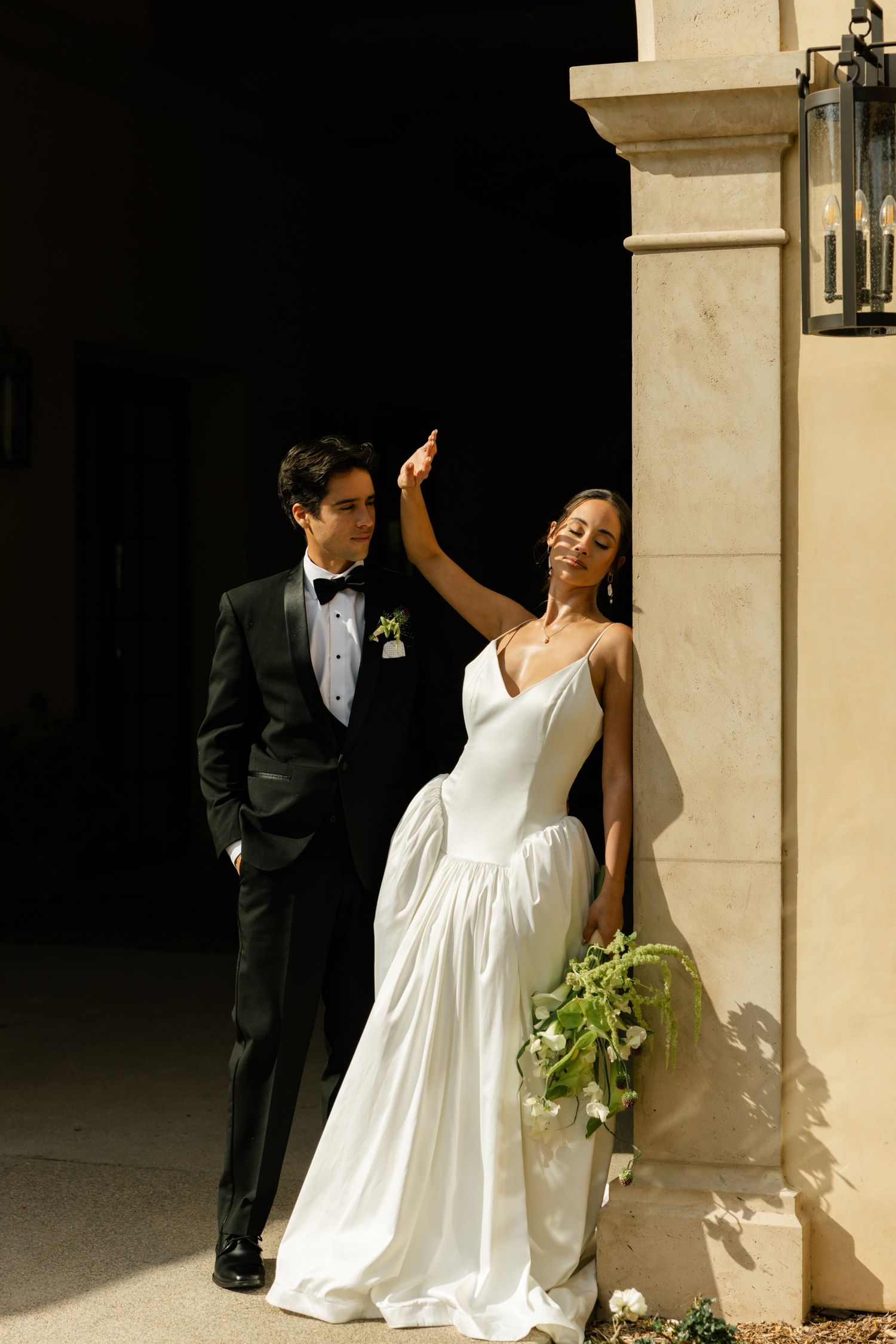 Dramatic wedding portrait against stone architecture with contrasting light and shadow.