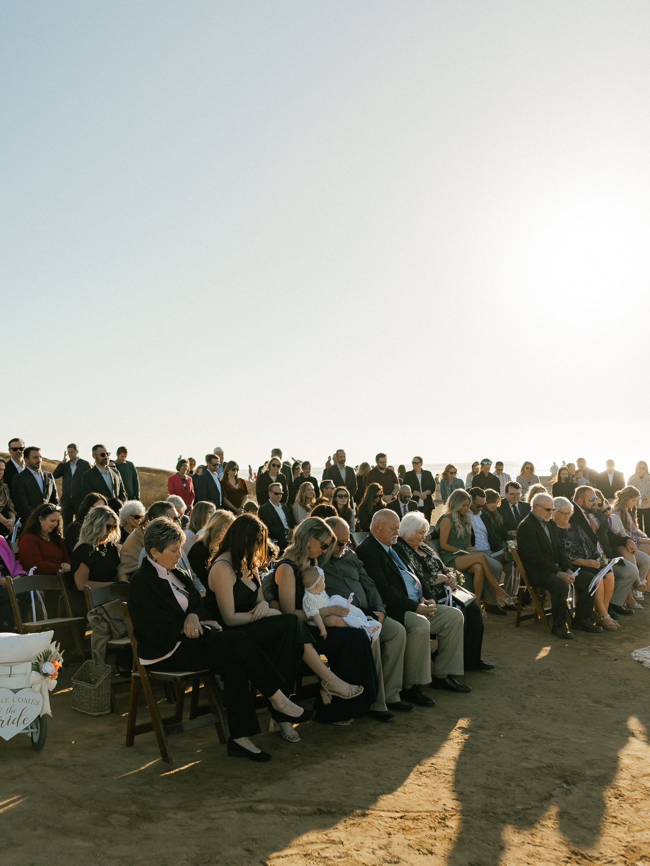 A large outdoor crowd seated in rows of chairs at a sunset ceremony.