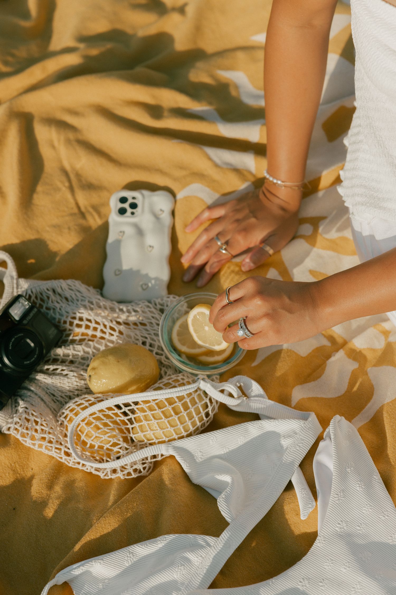 Hands arranging lemons on white lace fabric with iPhone and golden background in warm sunlight.