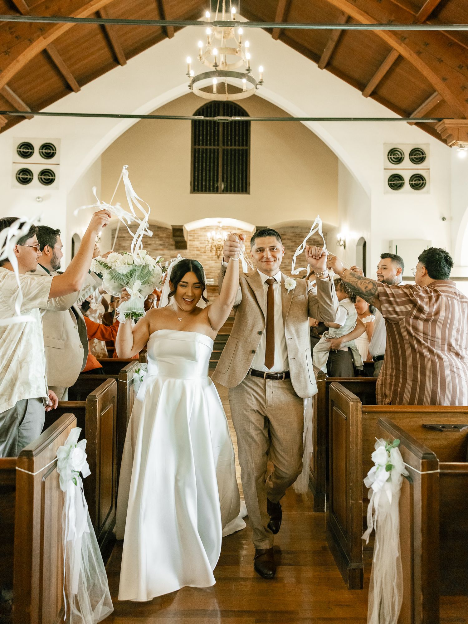 Wedding celebration in a charming chapel as guests raise streamers while the newlyweds walk down the aisle.