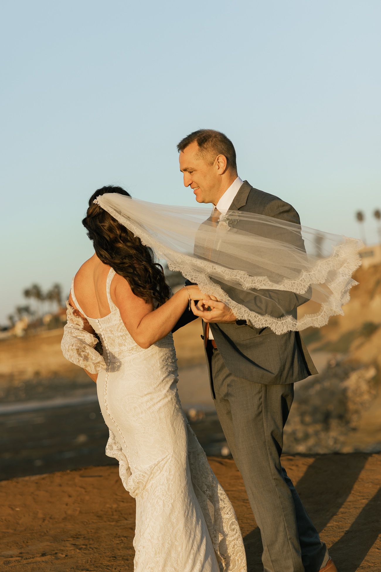 A couple dancing together outdoors with the bride's veil flowing in the wind during golden hour.