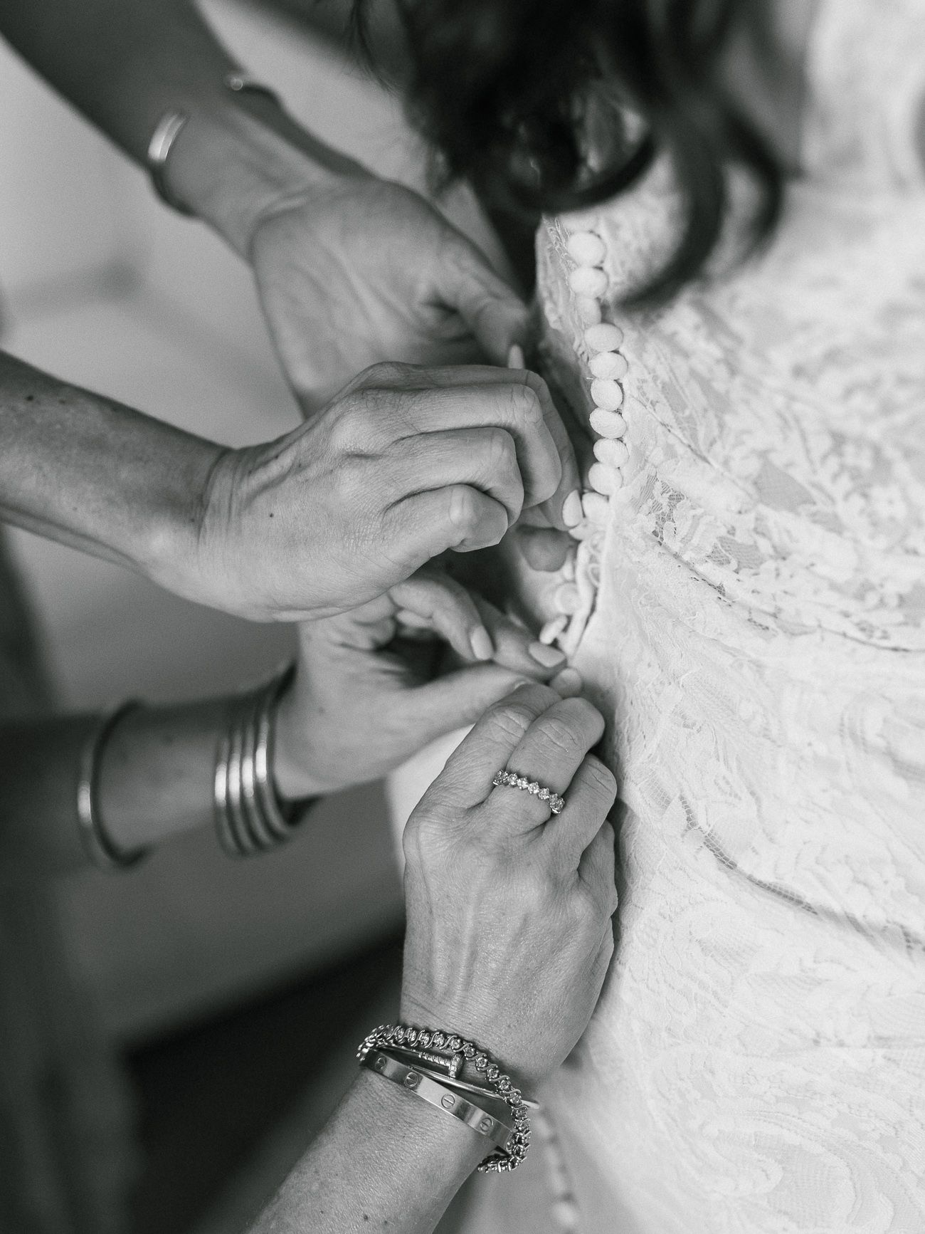 Close-up black and white photo of hands buttoning up a delicate lace wedding dress.