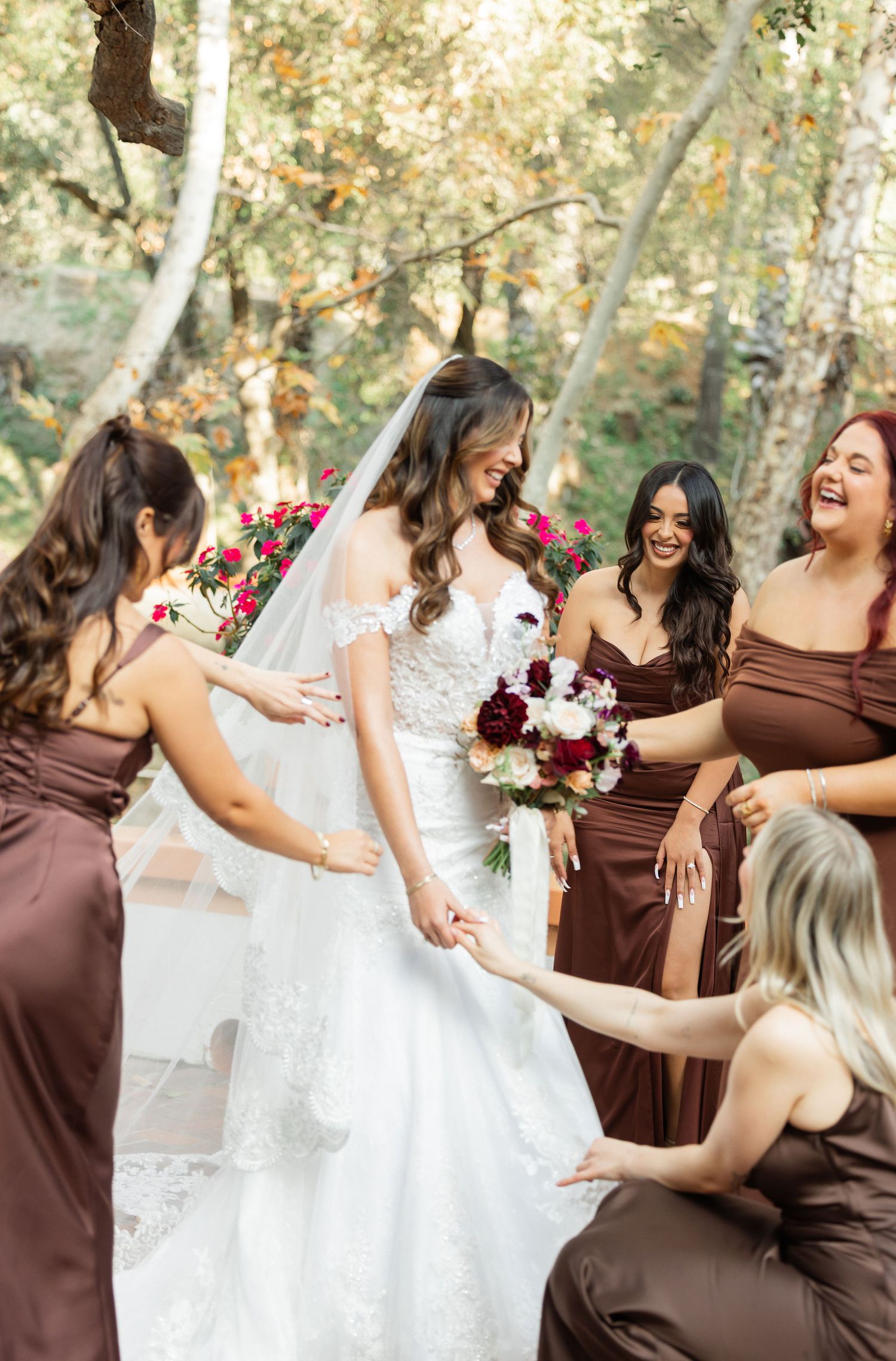 Bridesmaids in brown dresses and bride in white gown share joyful candid moments during outdoor wedding photo session.