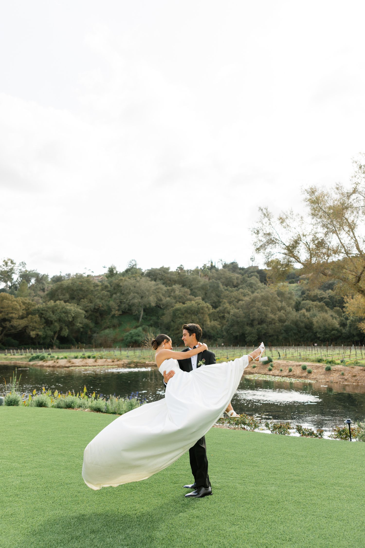 Romantic wedding photo of a couple on a manicured lawn with a pond in the background.